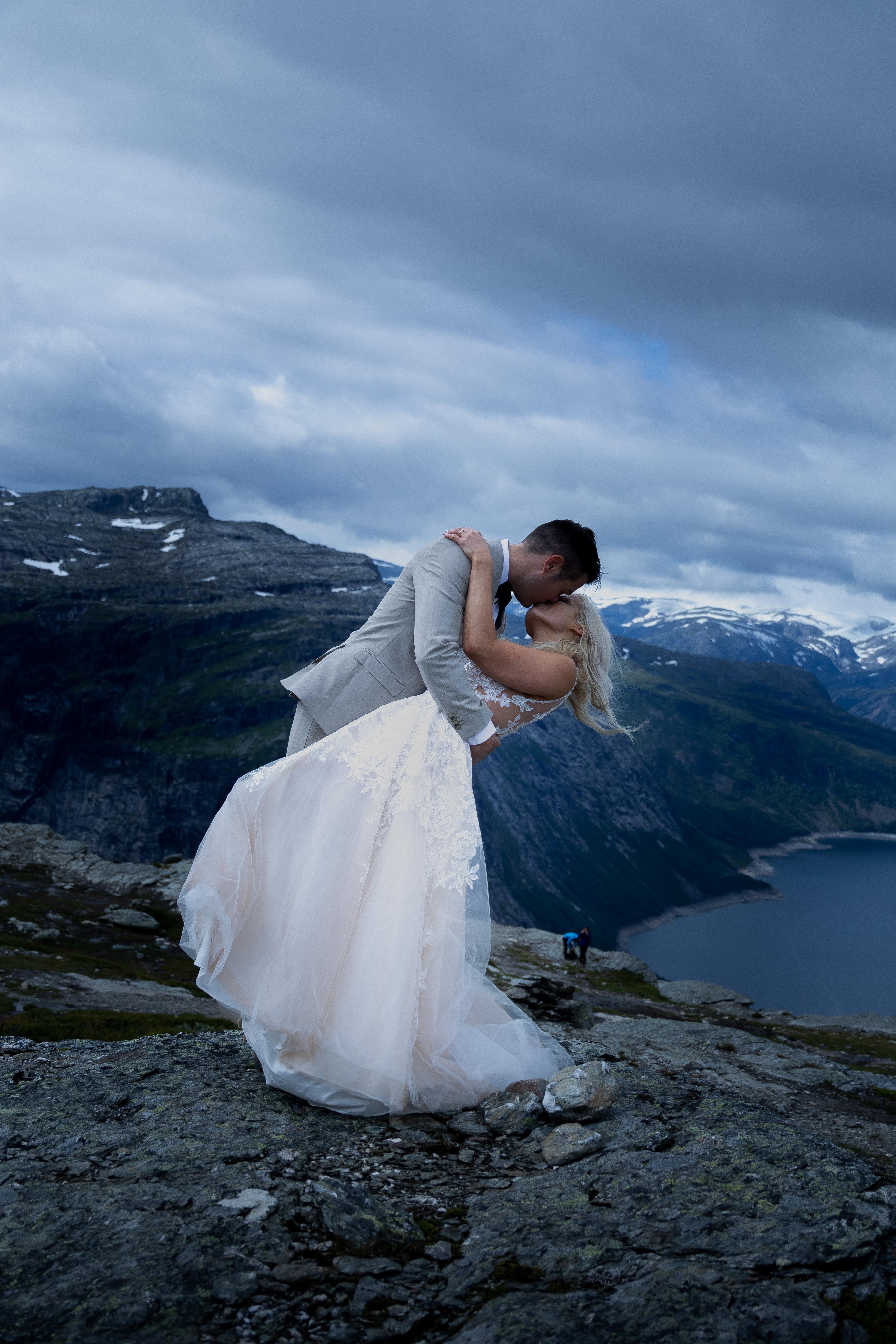 A newly wed couple kissing at the top of Trolltunga in Ullensvang in Fjord Norway