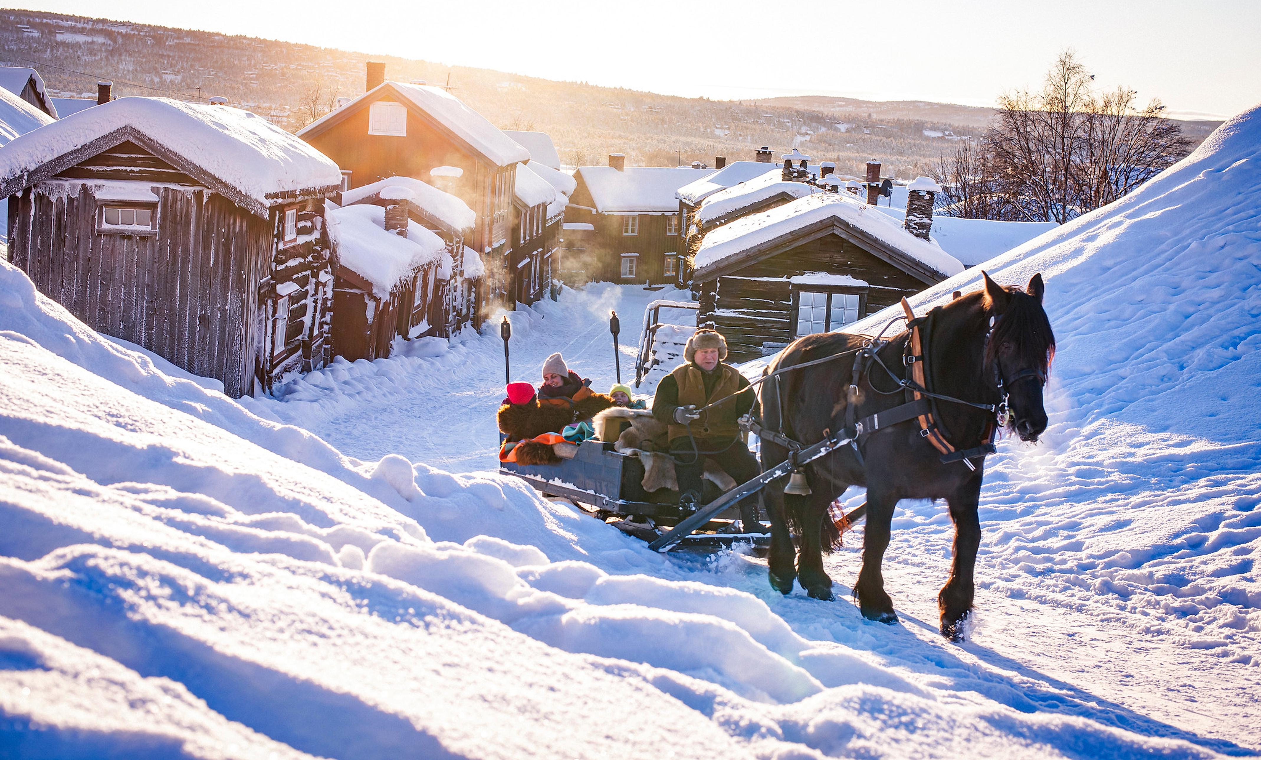 Tre personer kjører hest og slede på Røros en kald vinterdag