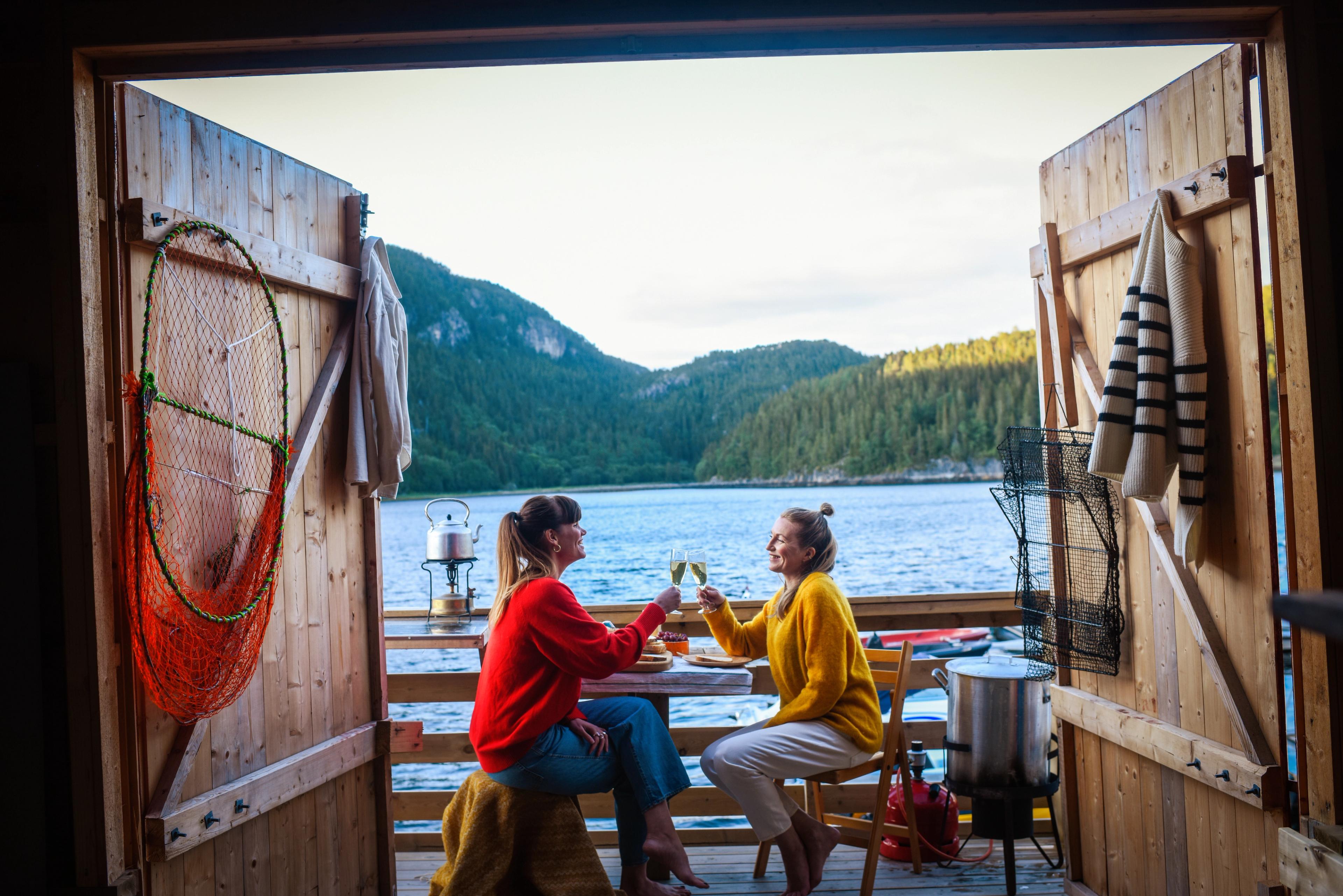 Two woman enjoying some drinks outside a fisherman's cabin by the sea