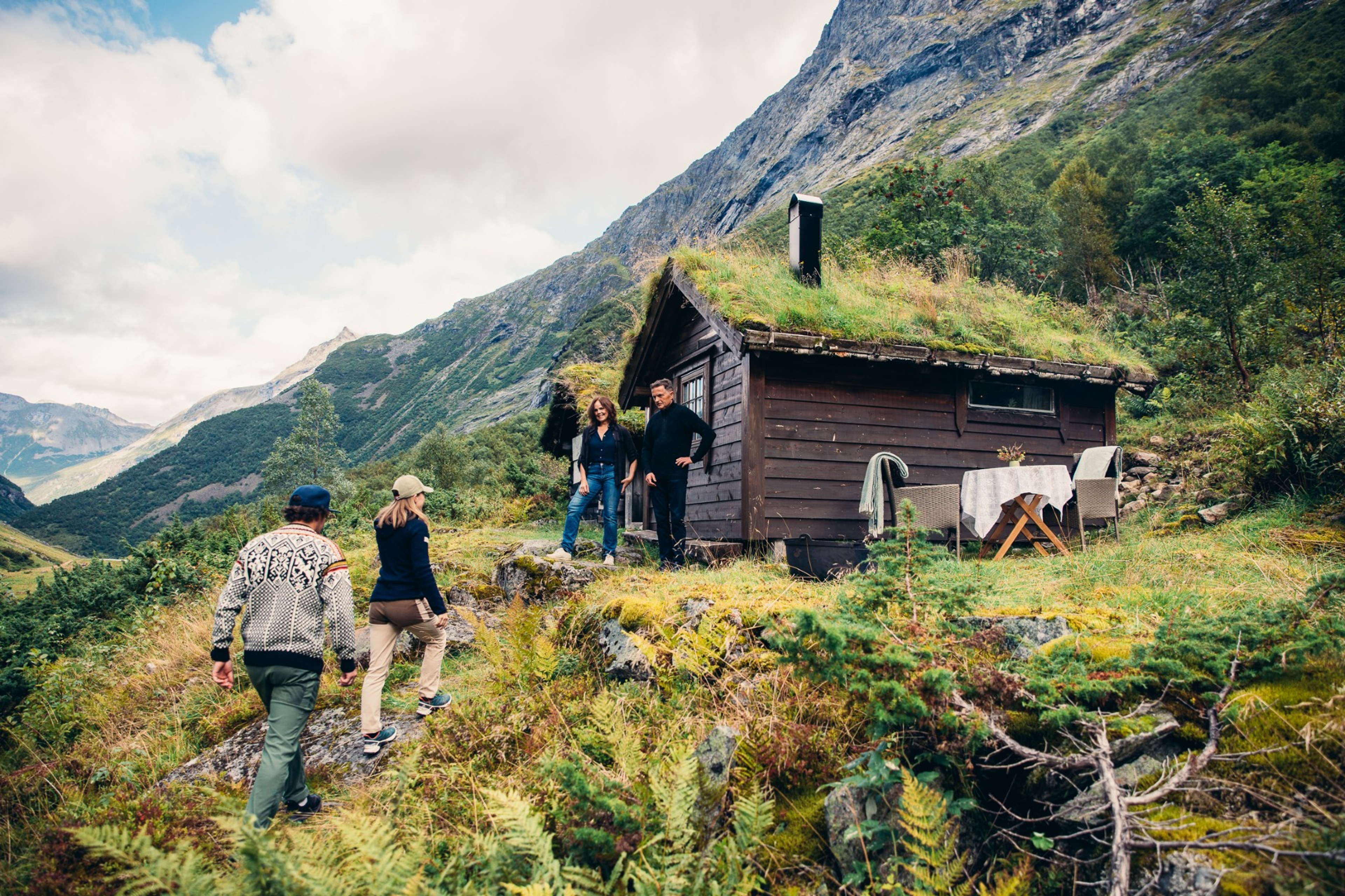 Hikers approaching a small wooden cabin with grass roof in mountainous landscape