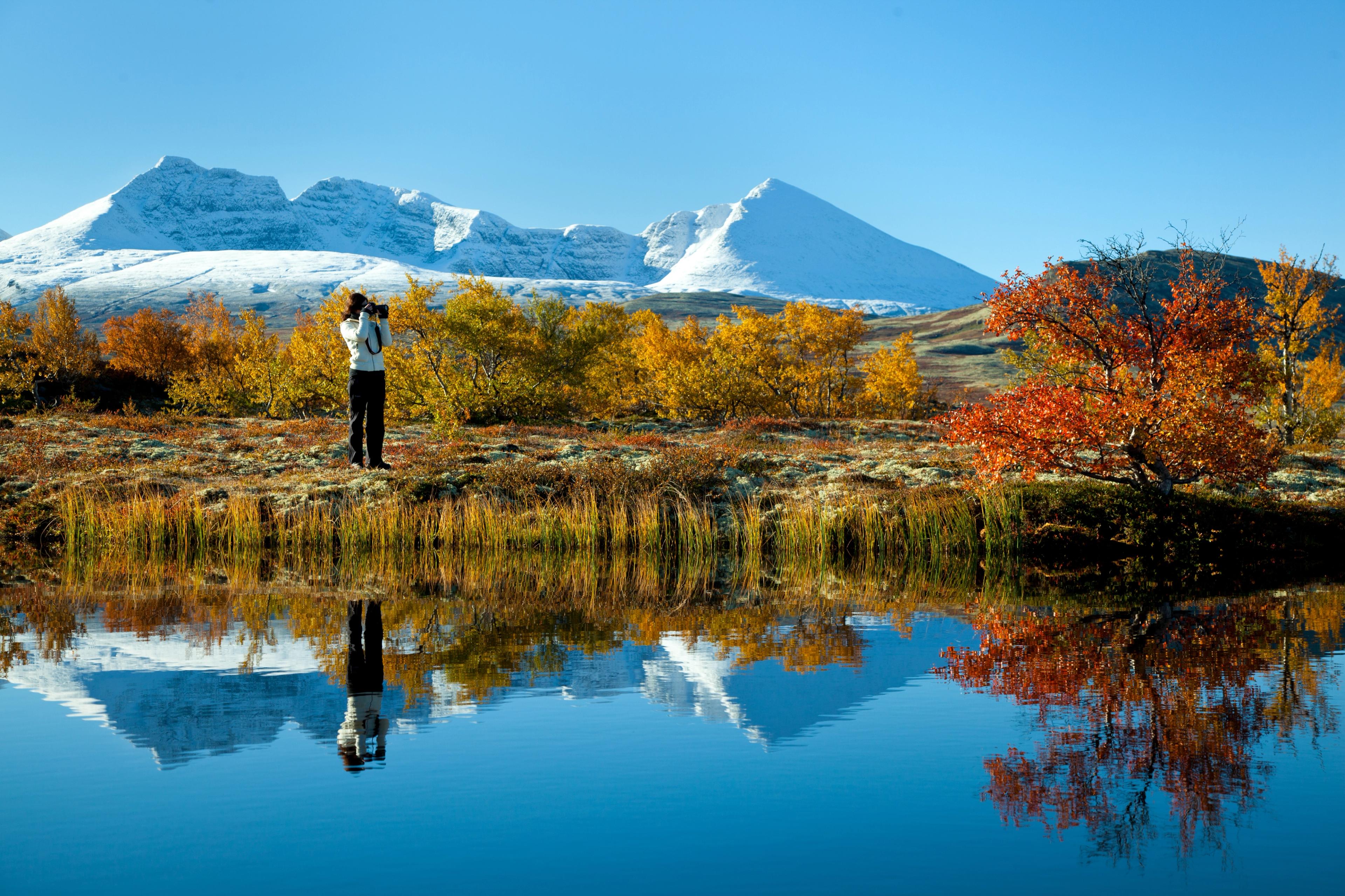 A woman taking pictures of a mountain and autumn landscape