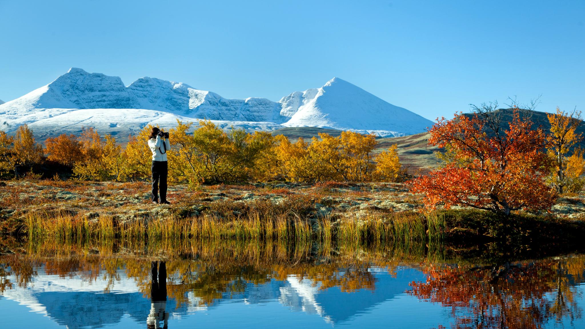 A woman taking pictures of a mountain and autumn landscape