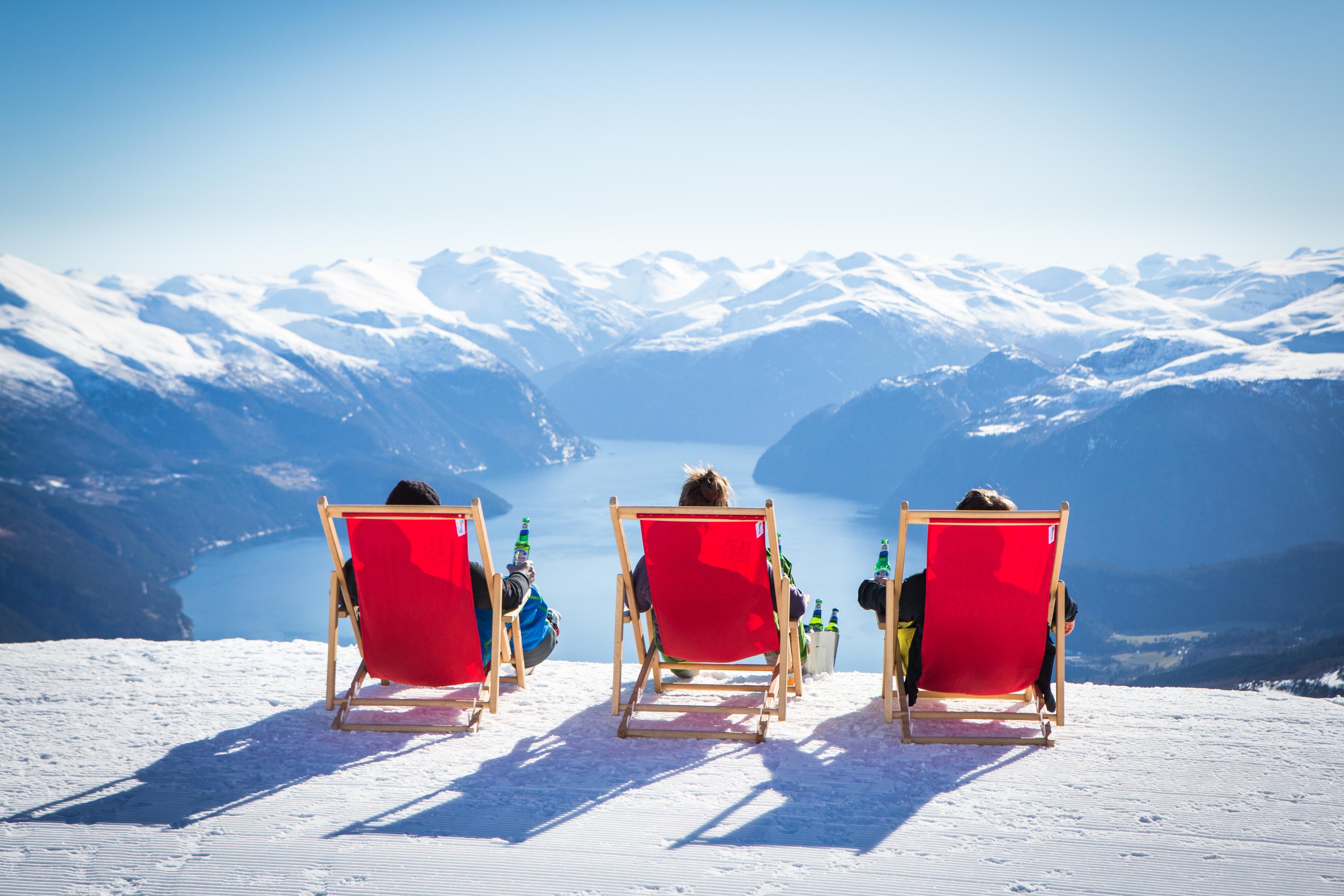 Three people in red deckchair on the top of the alpine slope at Strandafjellet in Fjord Norway