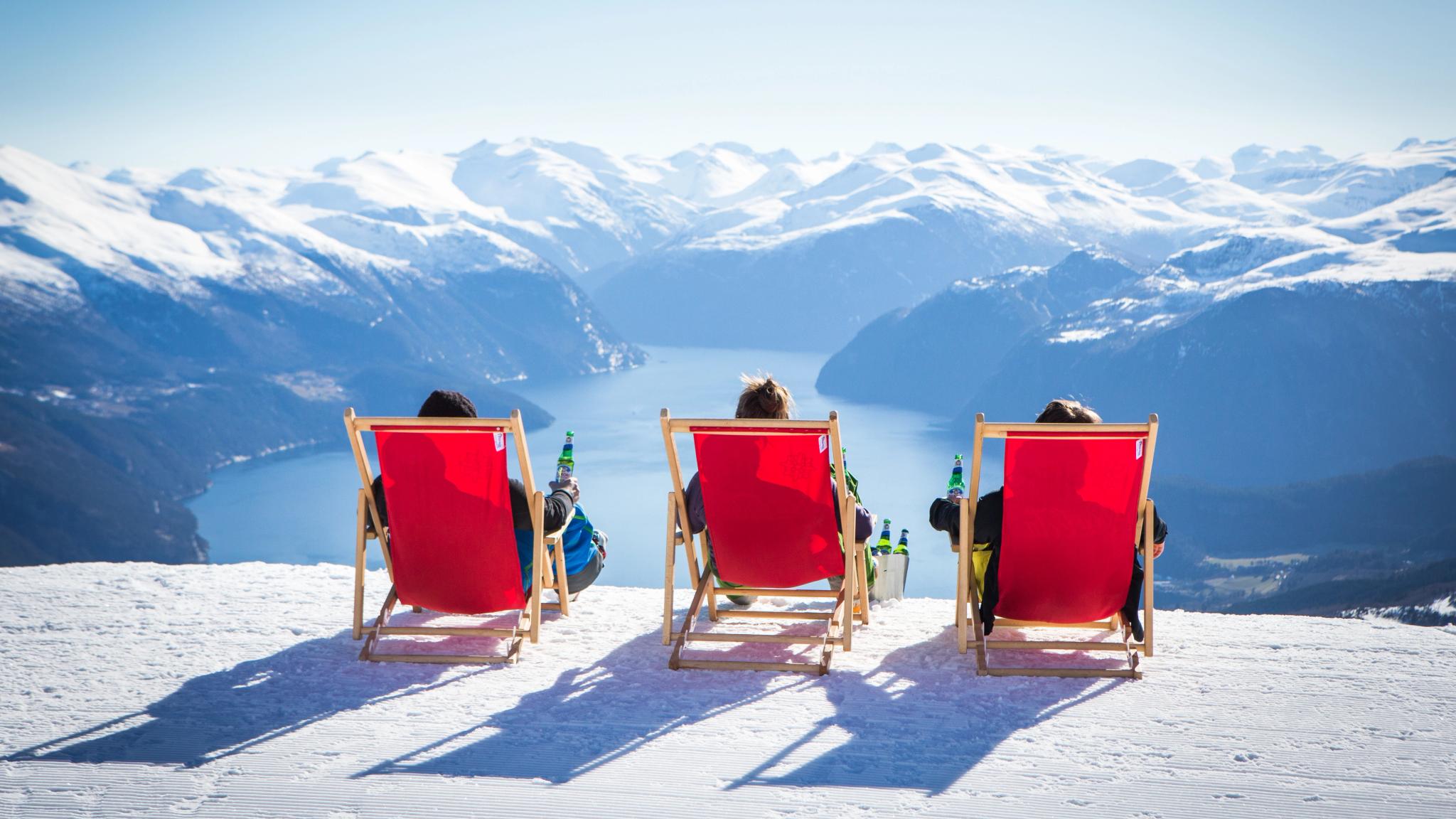 Three people in red deckchair on the top of the alpine slope at Strandafjellet in Fjord Norway