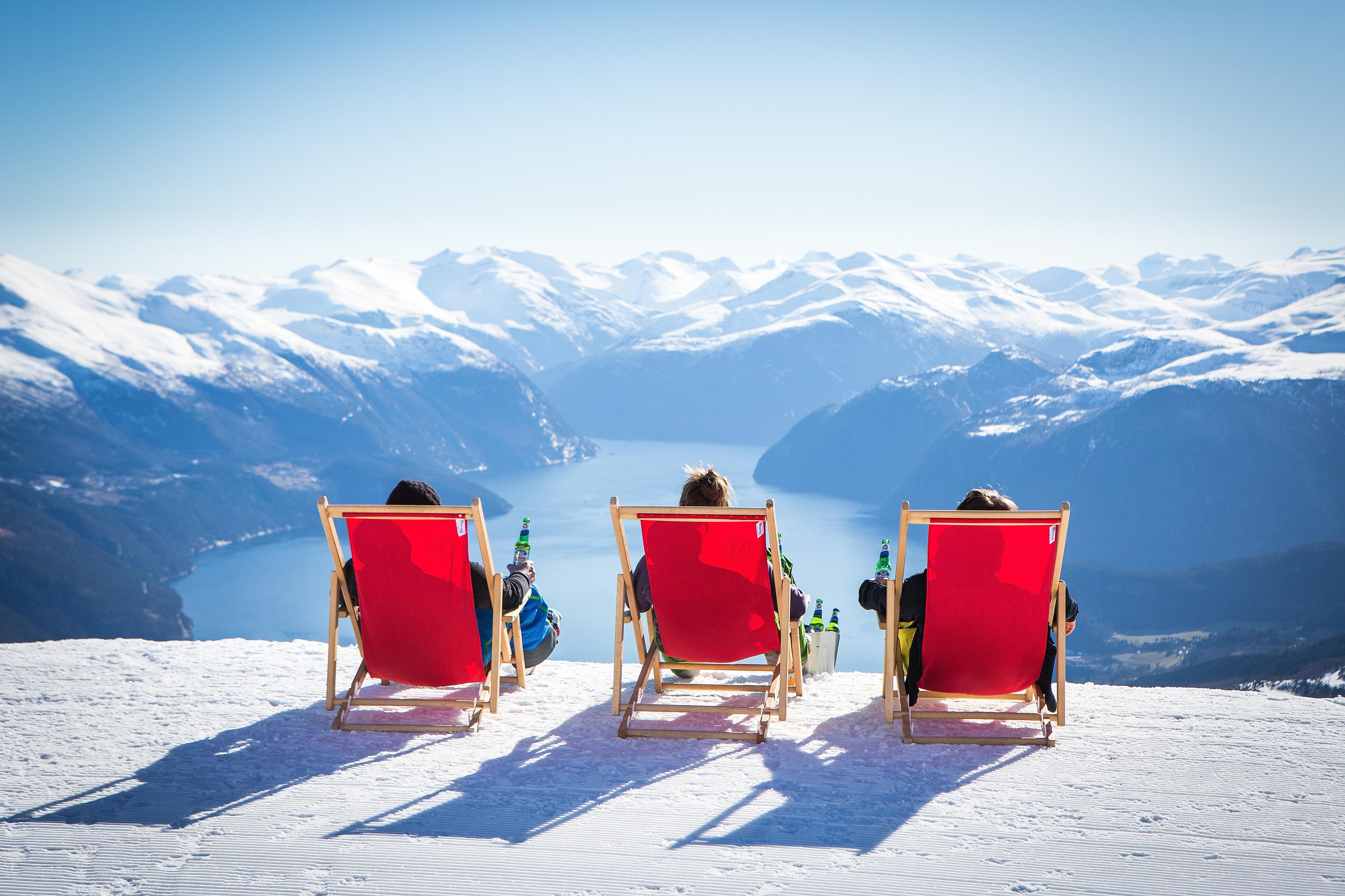 Three people in red deckchair on the top of the alpine slope at Strandafjellet in Fjord Norway