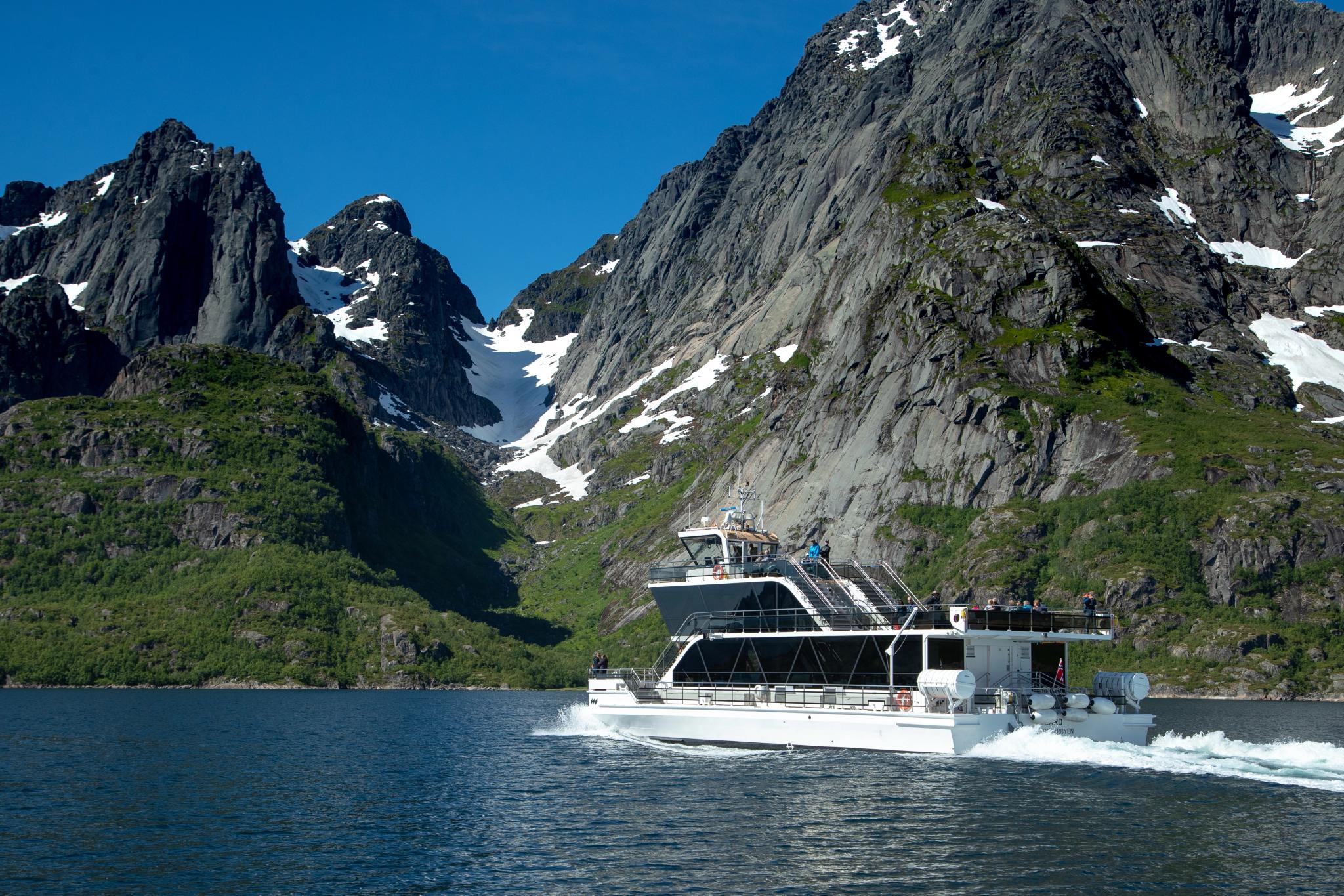 An electrical boat in the narrow Trollfjord in Lofoten under huge mountains.