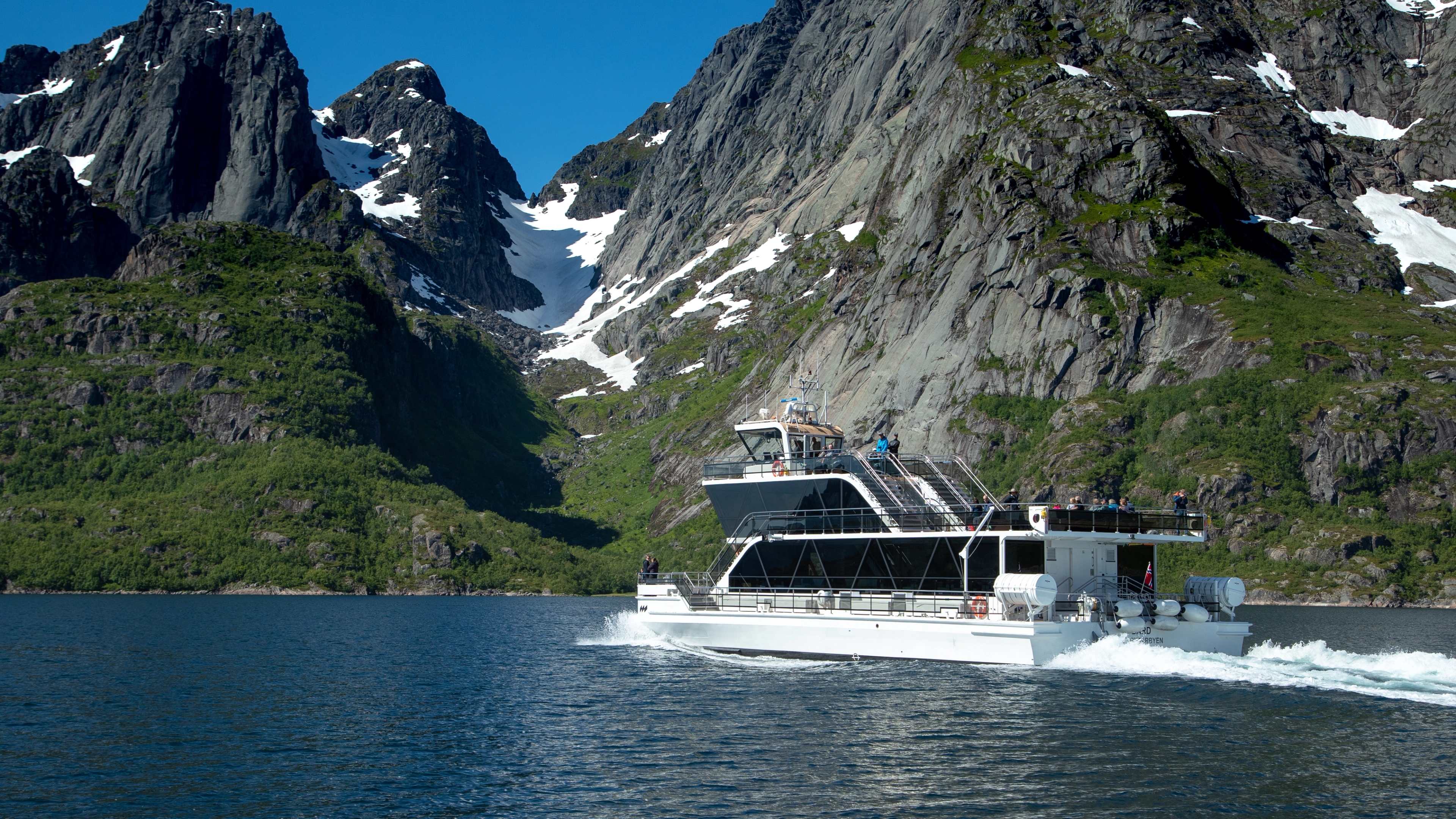 An electrical boat in the narrow Trollfjord in Lofoten under huge mountains.
