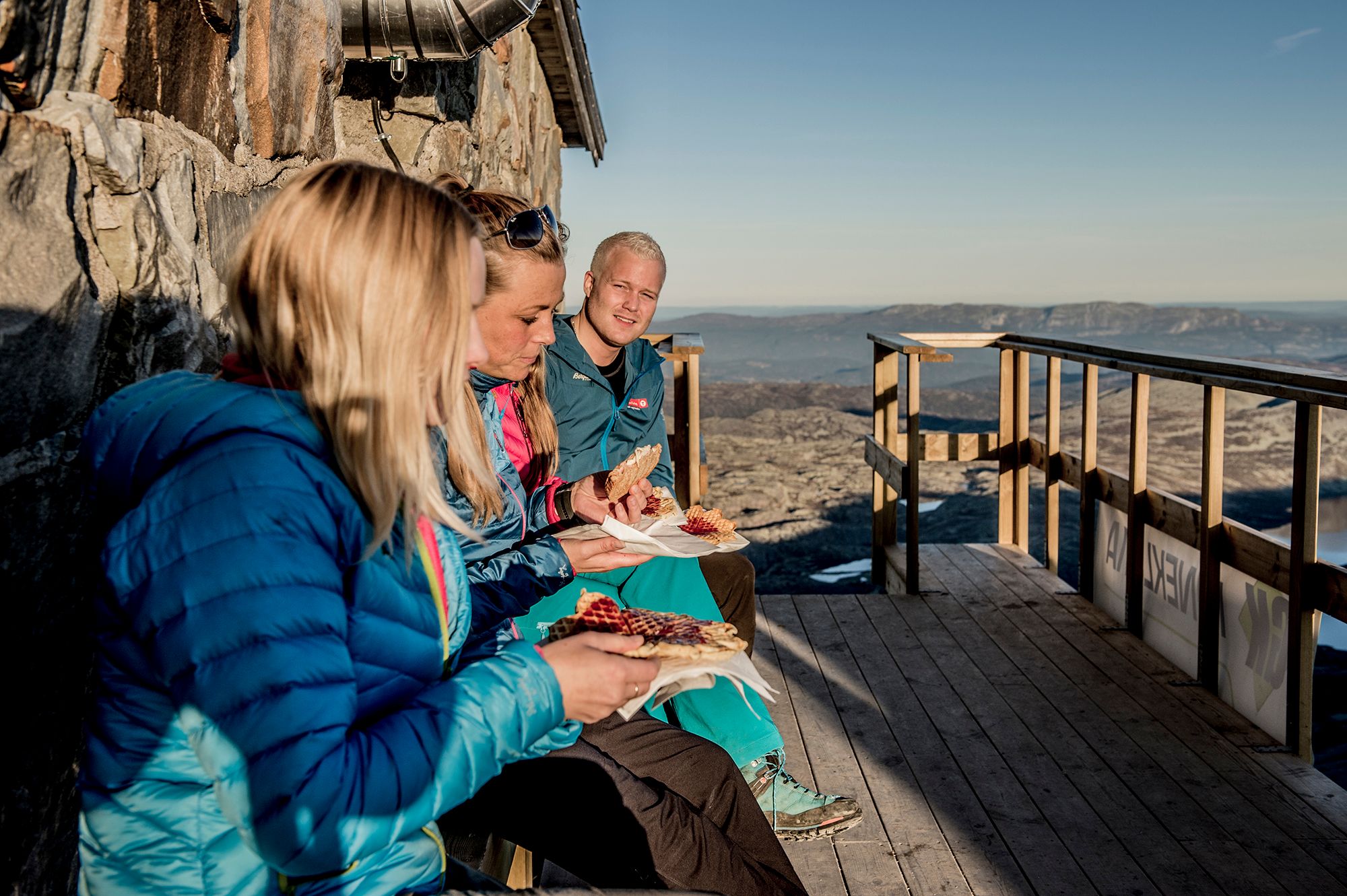 Tre mennesker spiser vafler utenfor Gaustatoppen turisthytte i Telemark