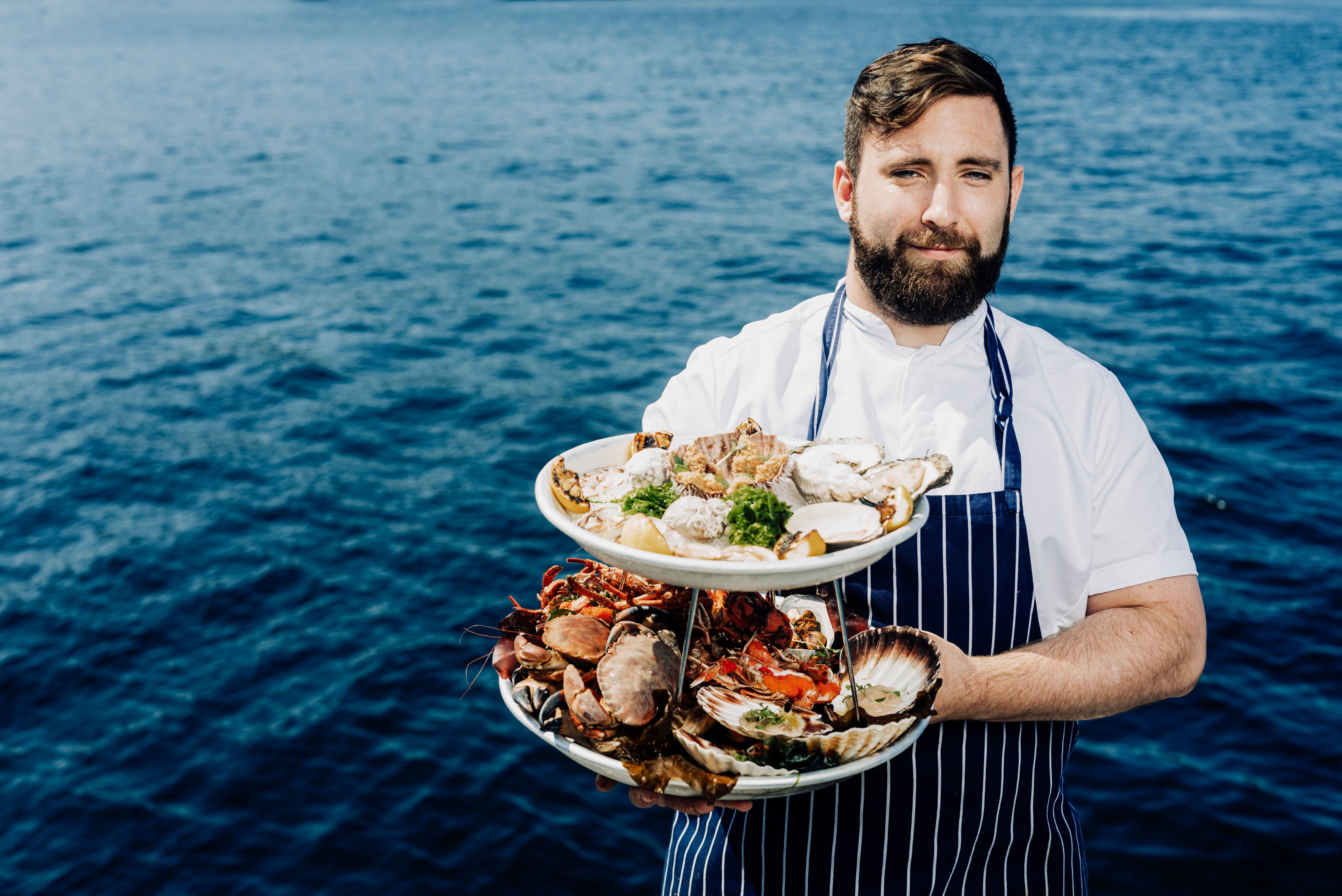 Man with shellfish dishes in front of the ocean.