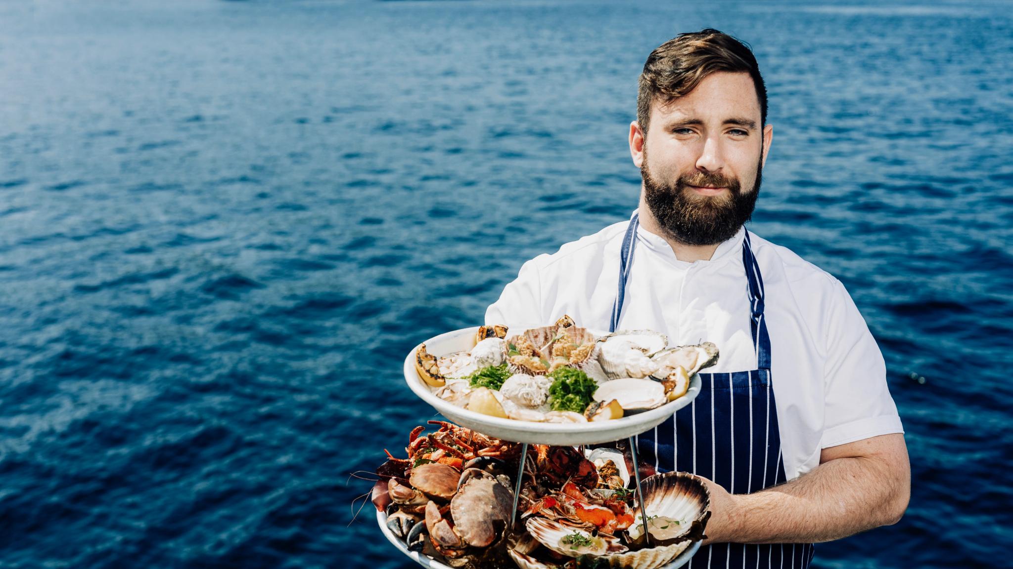 Man with shellfish dishes in front of the ocean.
