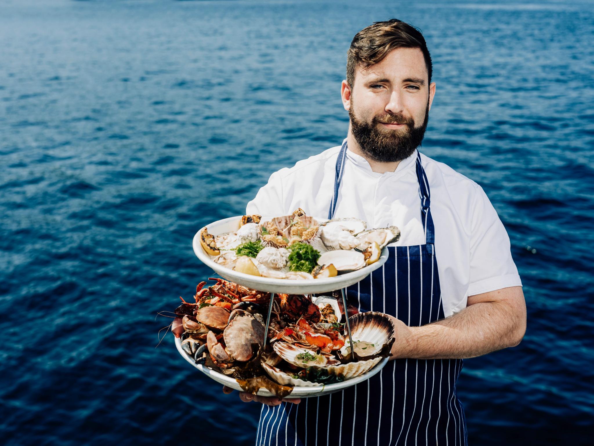 Man with shellfish dishes in front of the ocean.