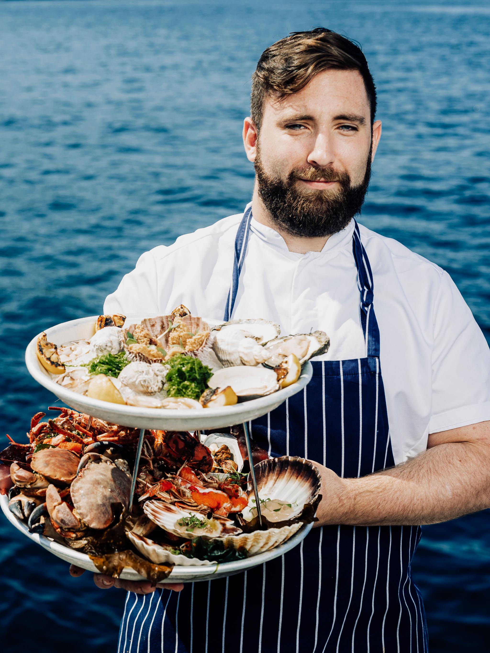 Man with shellfish dishes in front of the ocean.