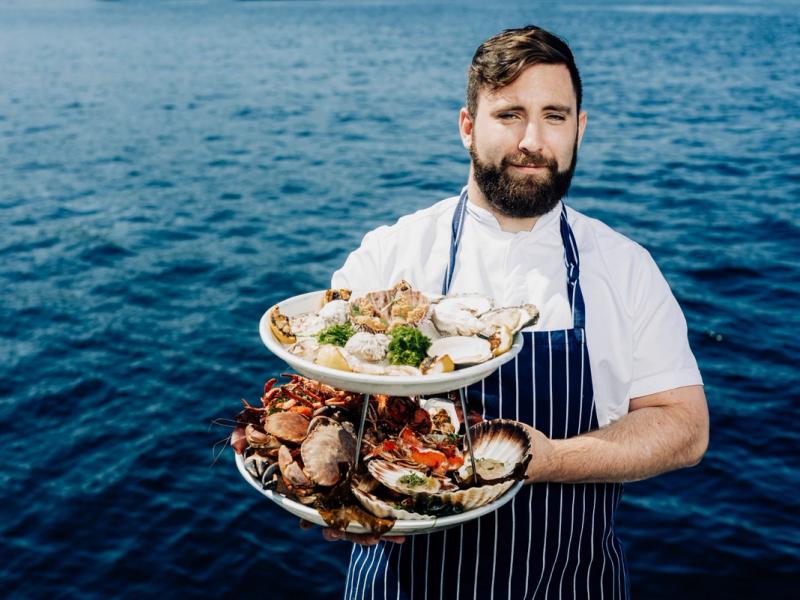 Man with shellfish dishes in front of the ocean.