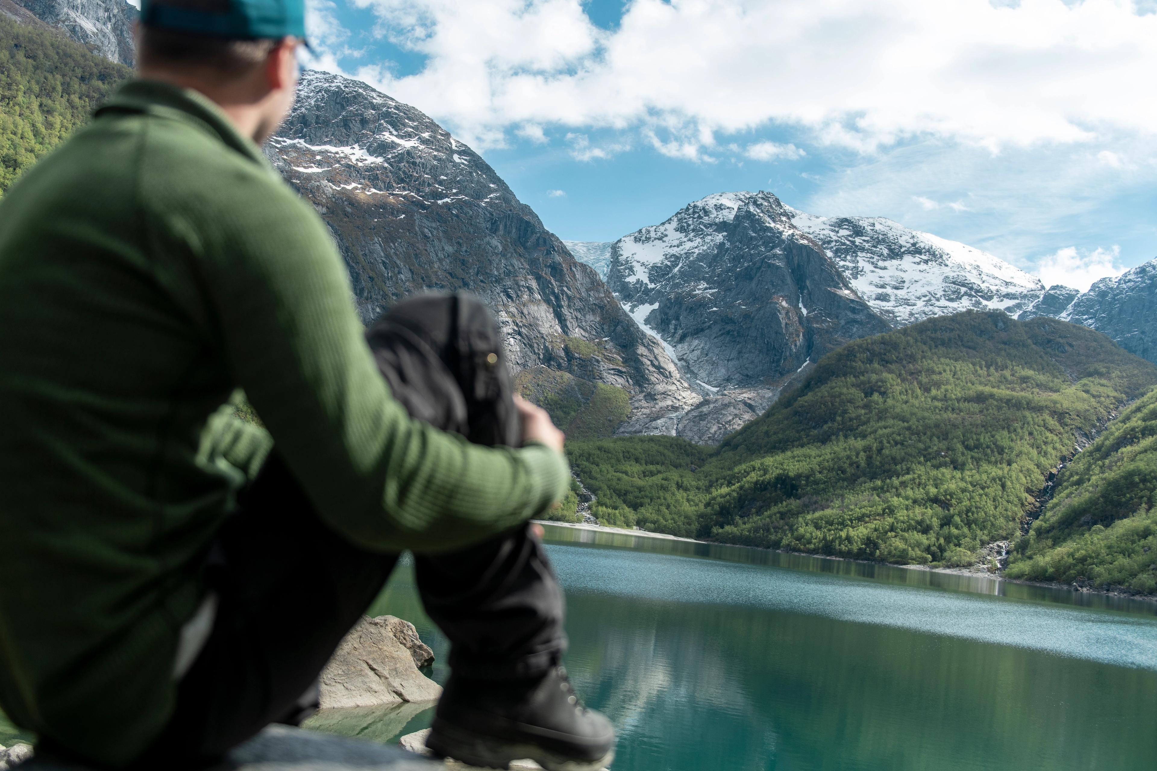A man looking at a clear lake and mountains.