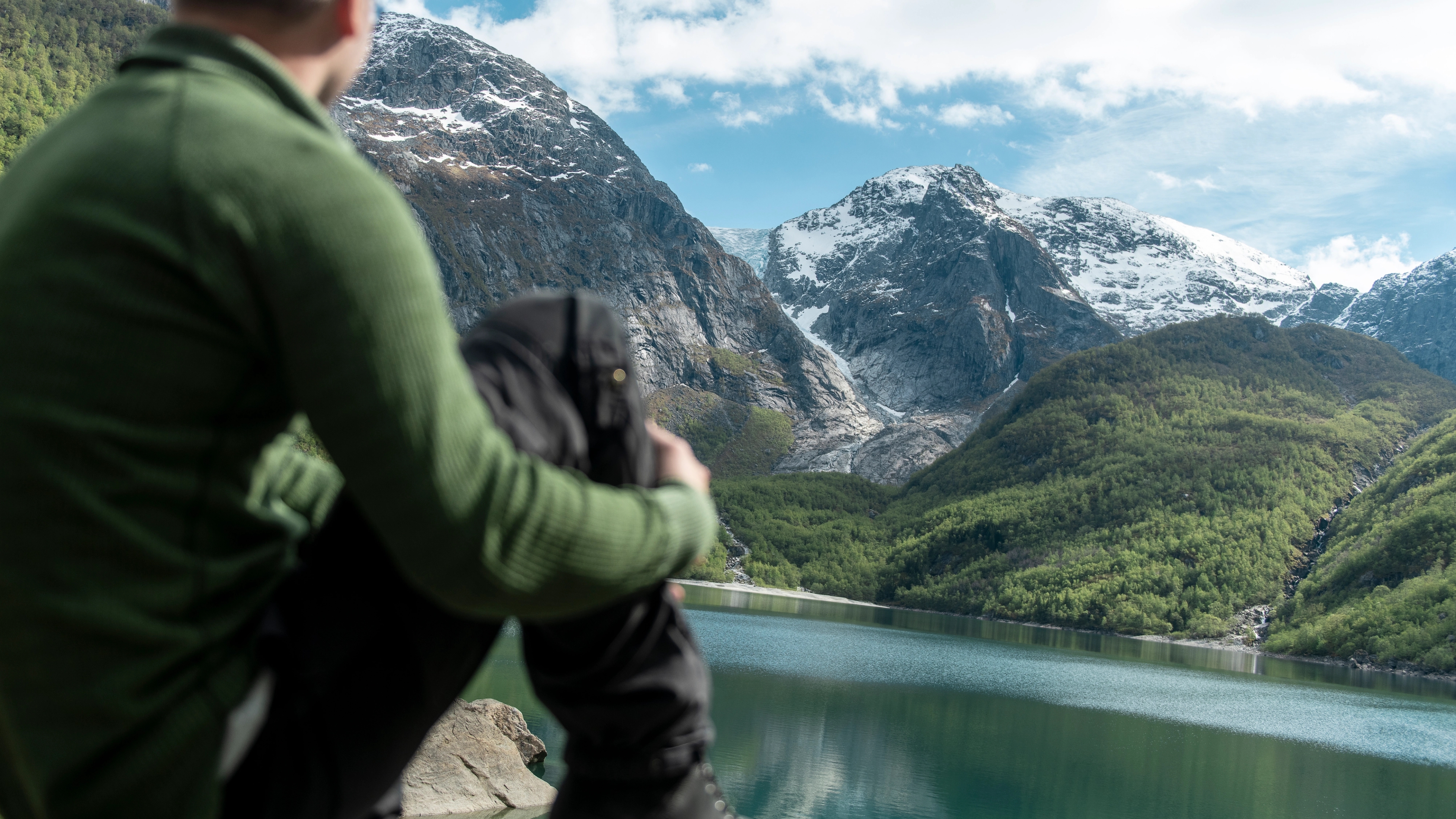 A man looking at a clear lake and mountains.