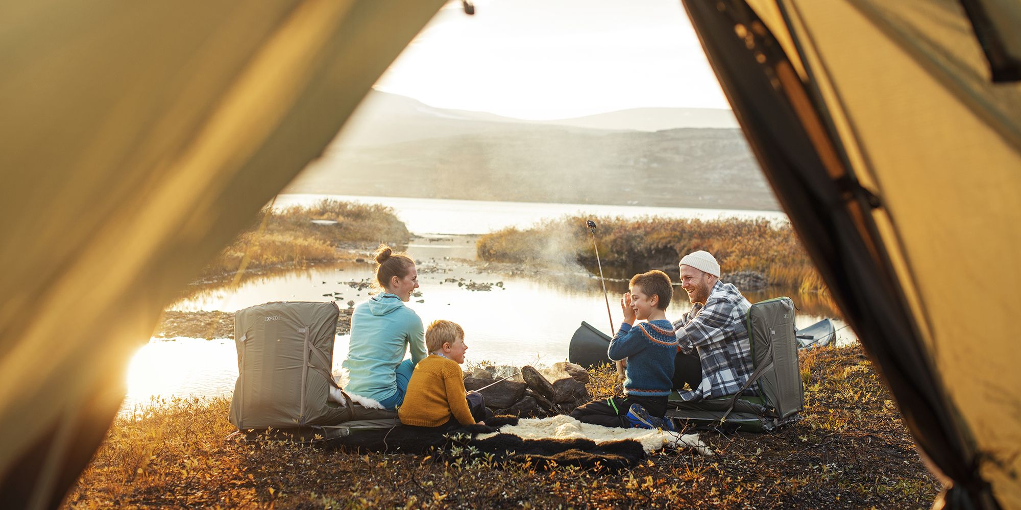 Family on four sitting by the campfire beside the tent in Oppdal, Trøndelag