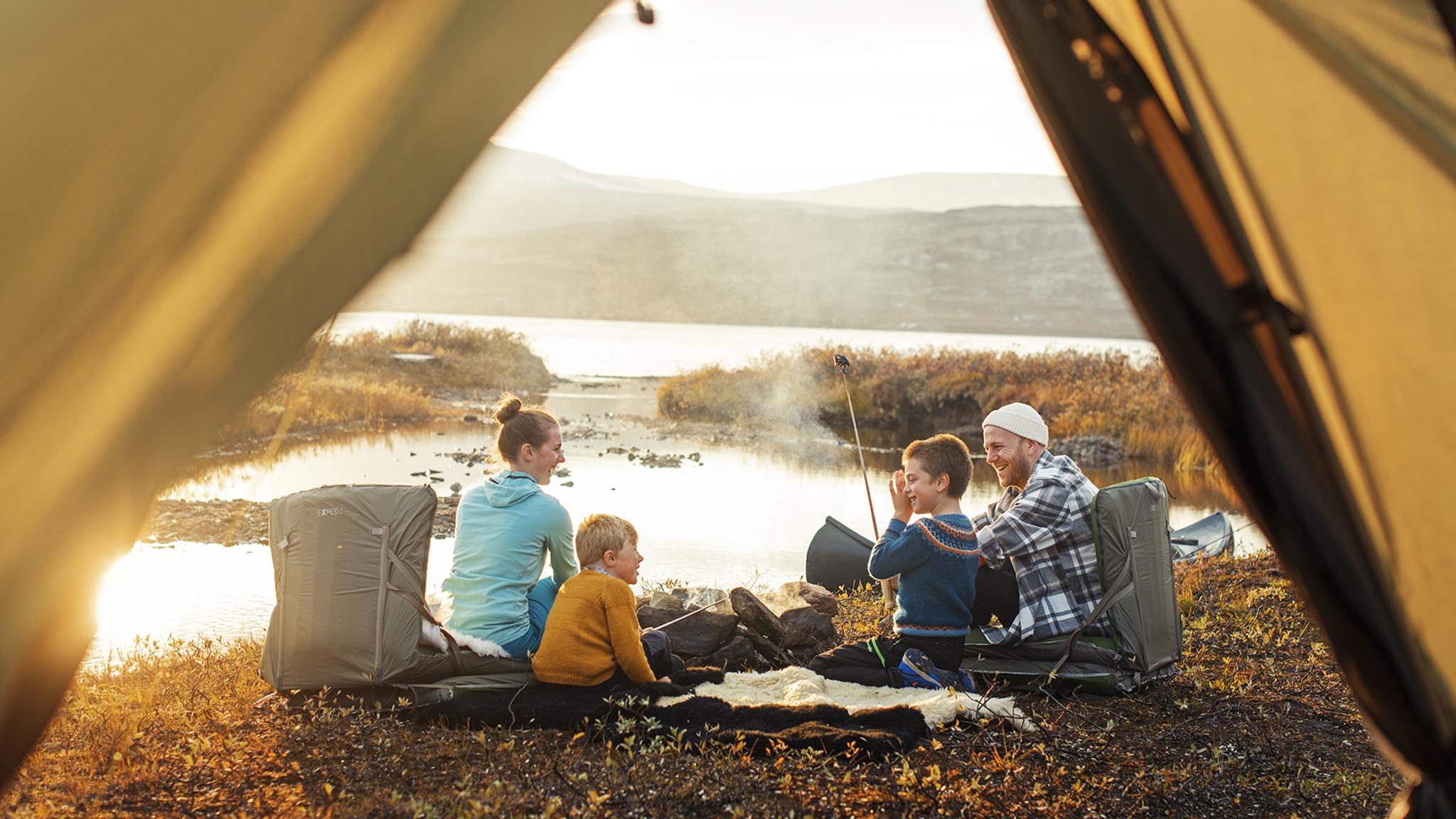 Family on four sitting by the campfire beside the tent in Oppdal, Trøndelag