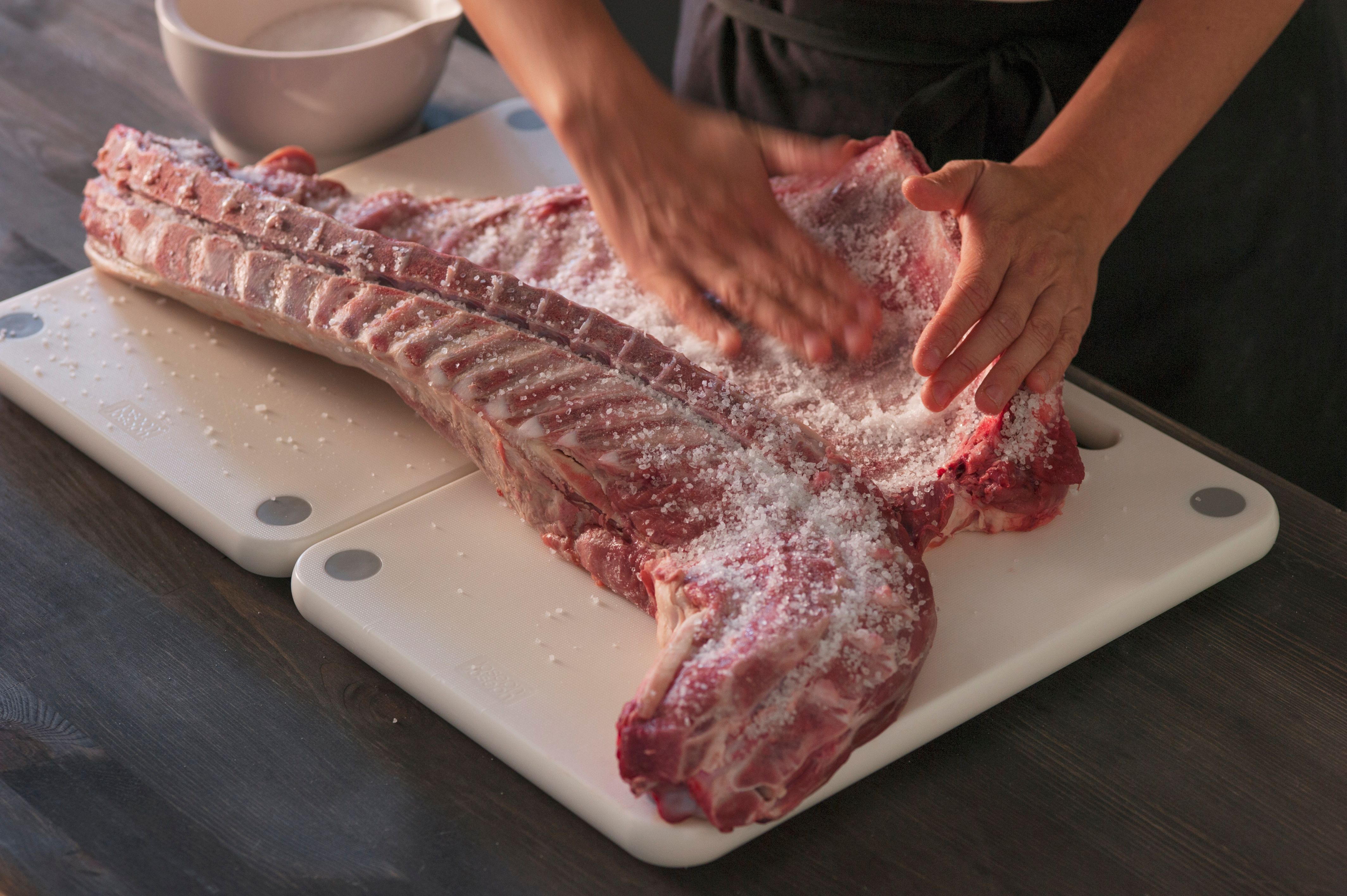 A woman salting lamb ribs.