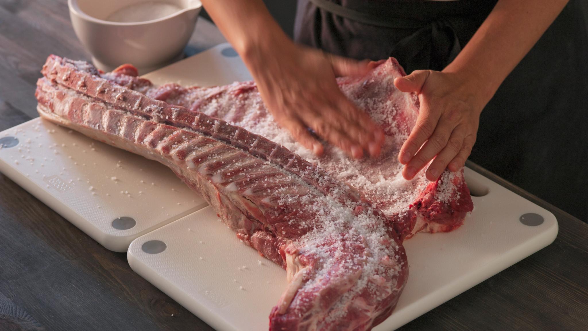 A woman salting lamb ribs.