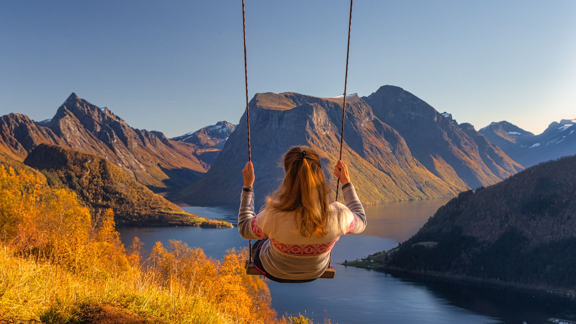 A woman on a swing with a scenic view to the Hjørundfjord and the famous Slogen mountain.