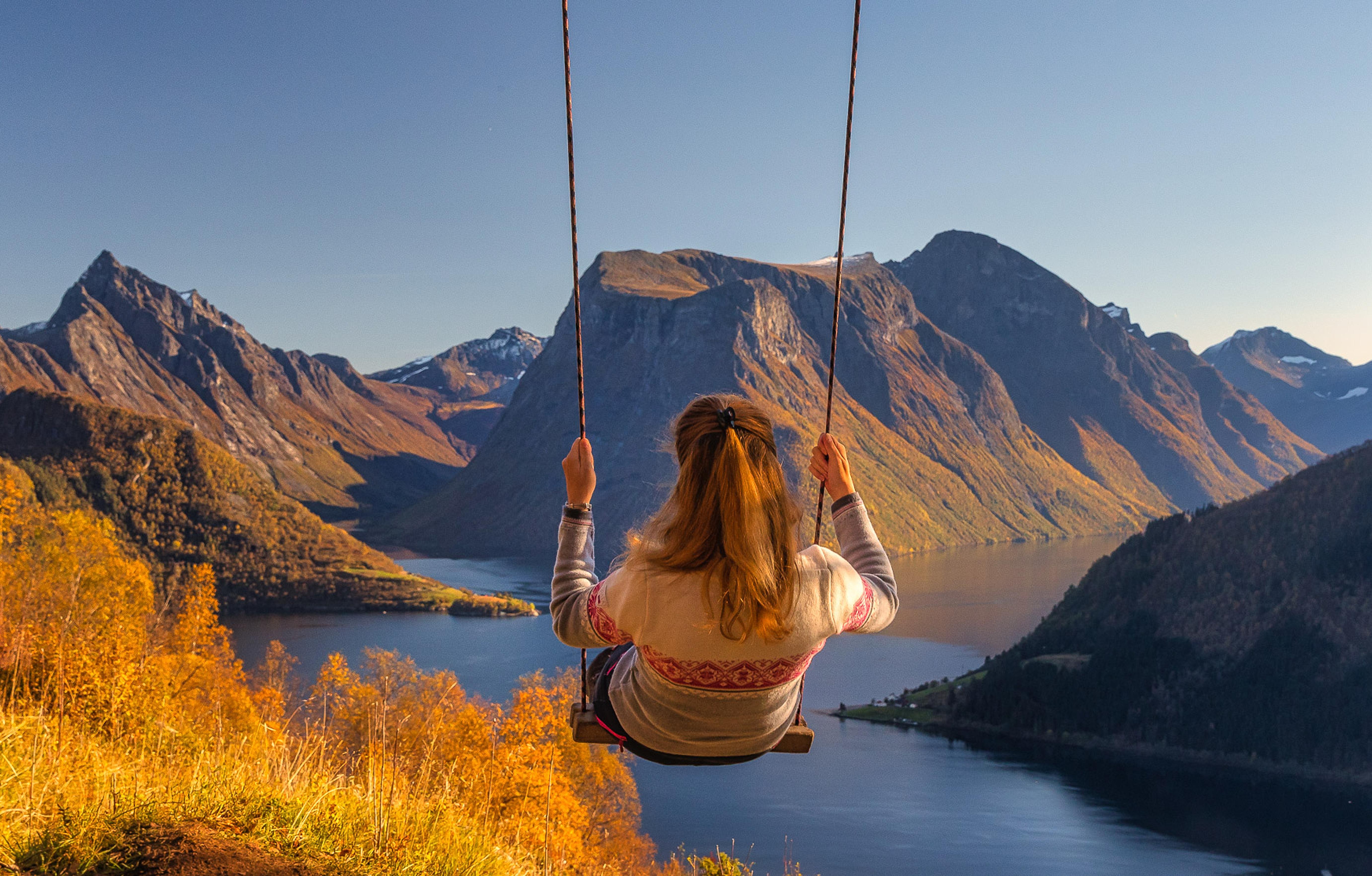 A woman on a swing with a scenic view to the Hjørundfjord and the famous Slogen mountain.
