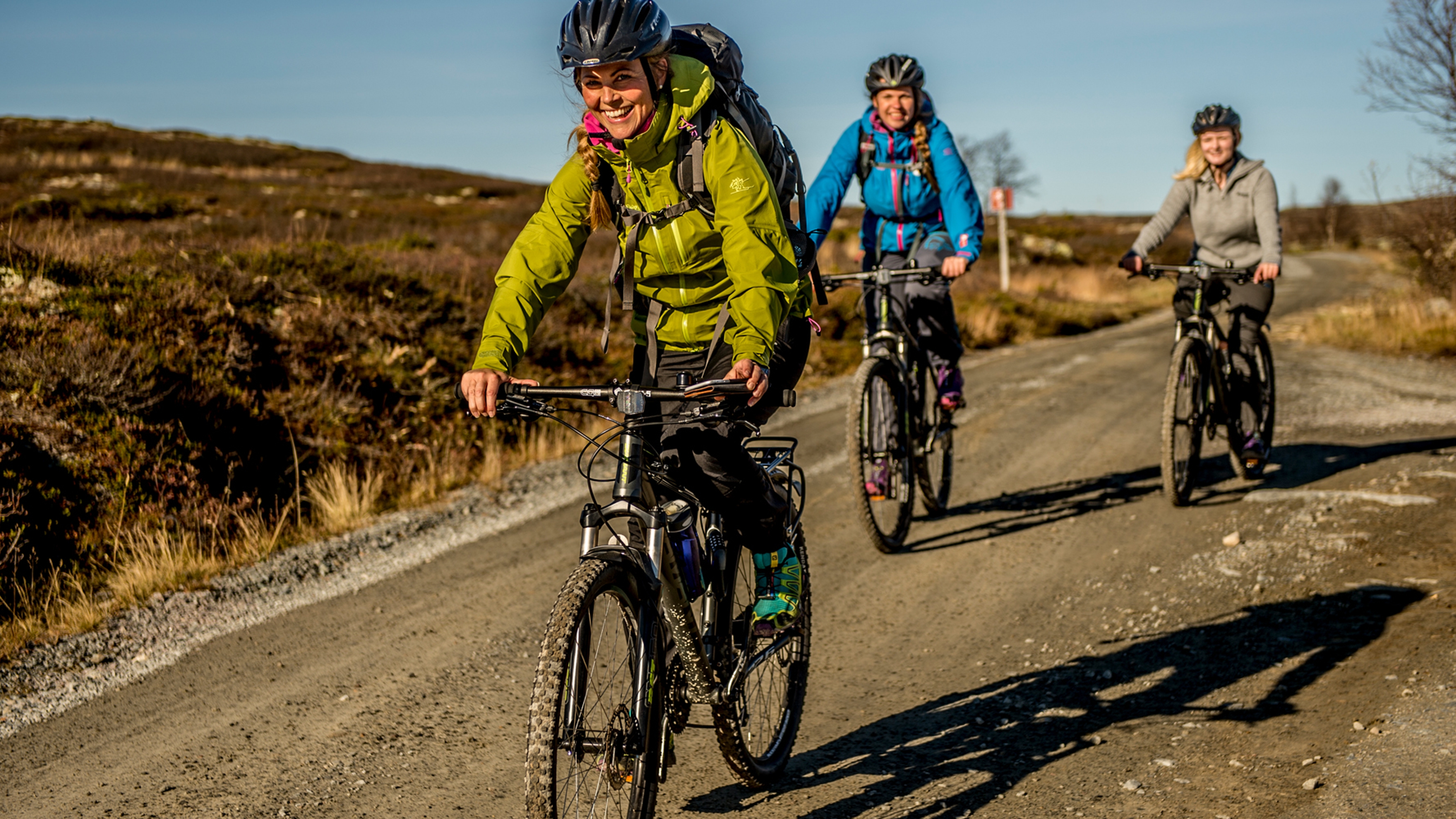 Three people cycling at a dirt road on the Hardangervidda mountain plateau in Eastern Norway