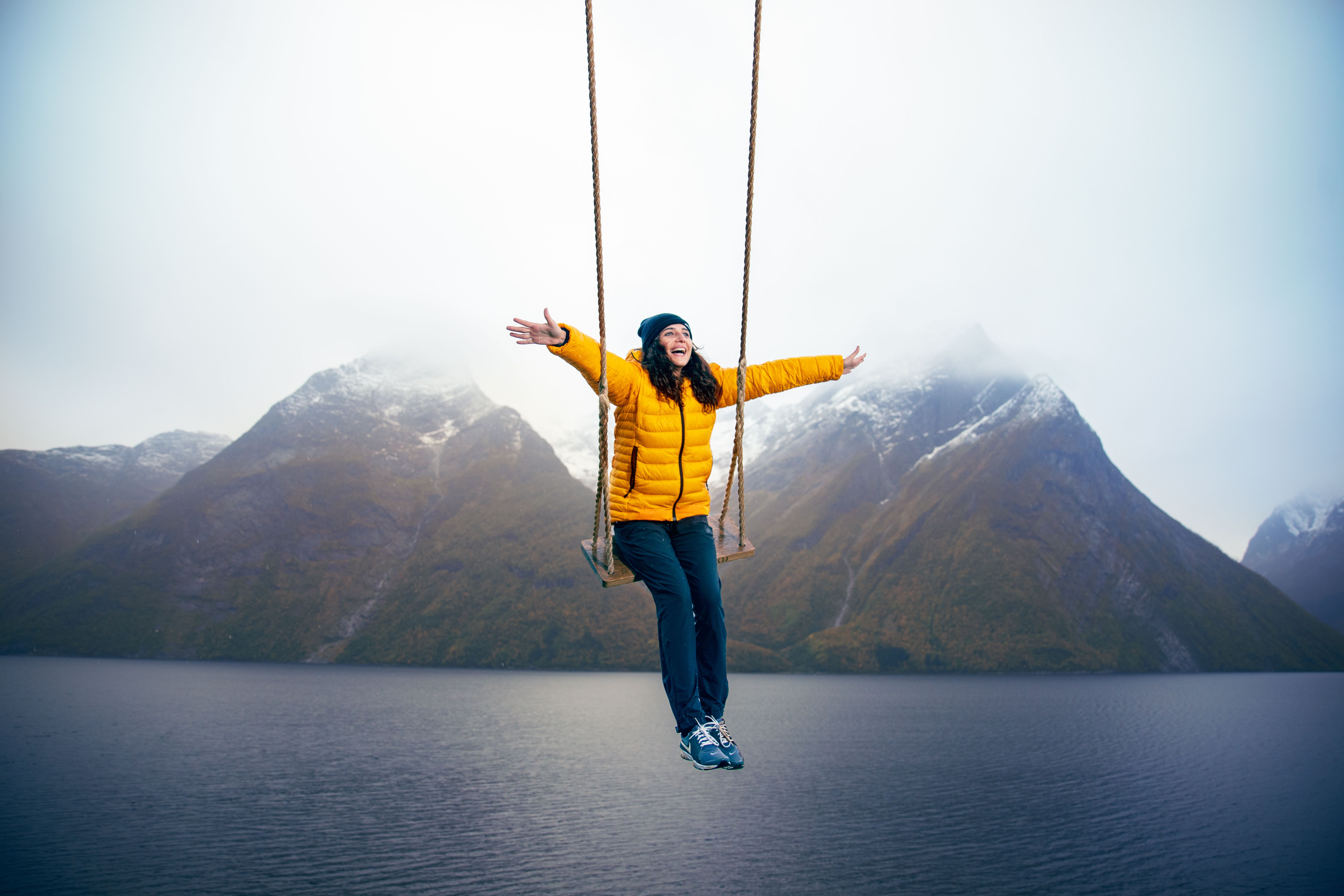 A person on a swing with a view of snow-clad mountains and the Hjørundfjord in Fjord Norway