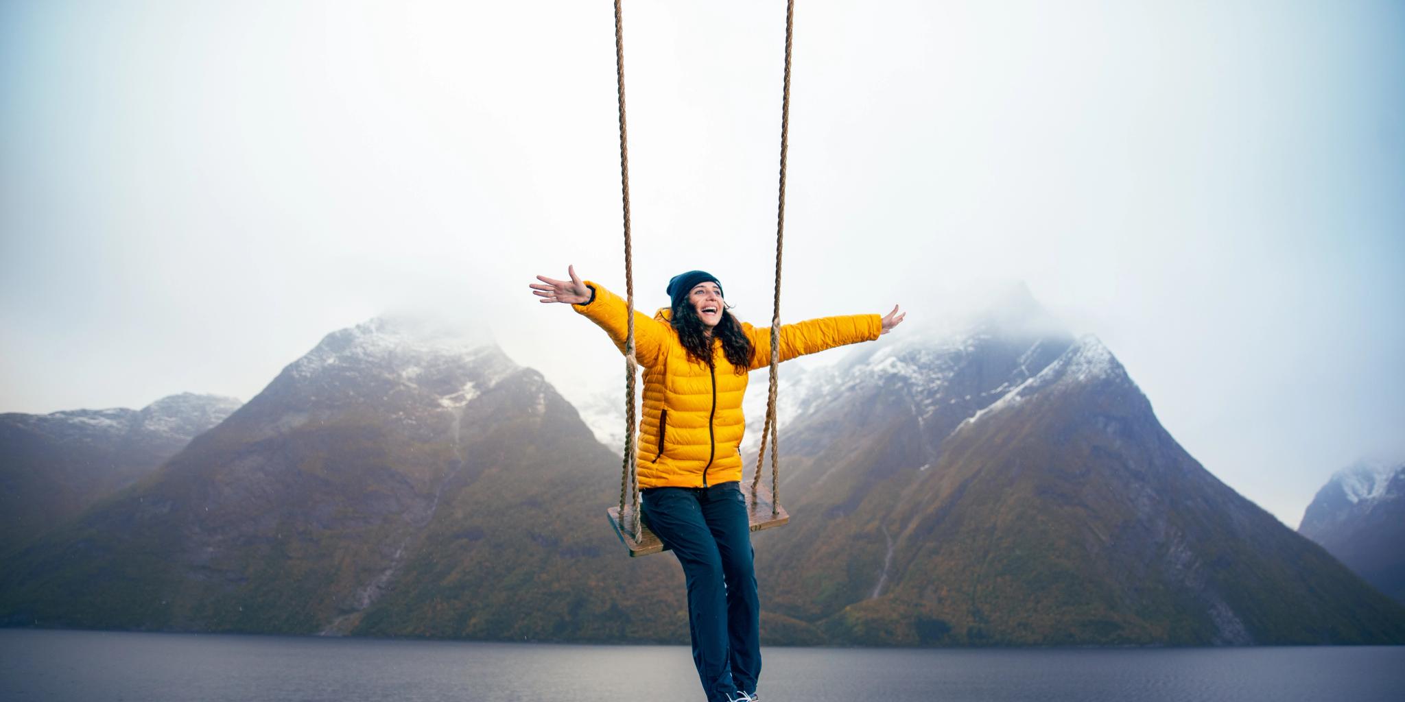 Eine Person auf einer Schaukel mit Blick auf schneebedeckte Berge und den Hjørundfjord in Fjord Norwegen