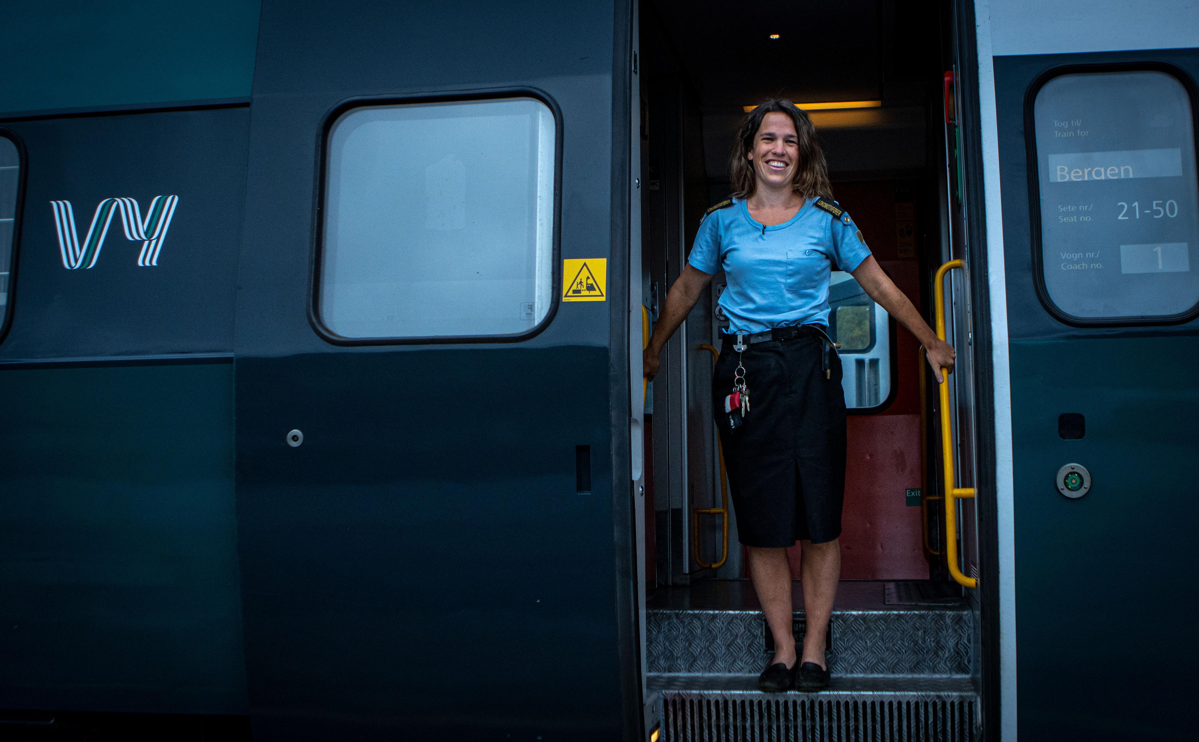 A train driver is standing at the entrance to a train wagon