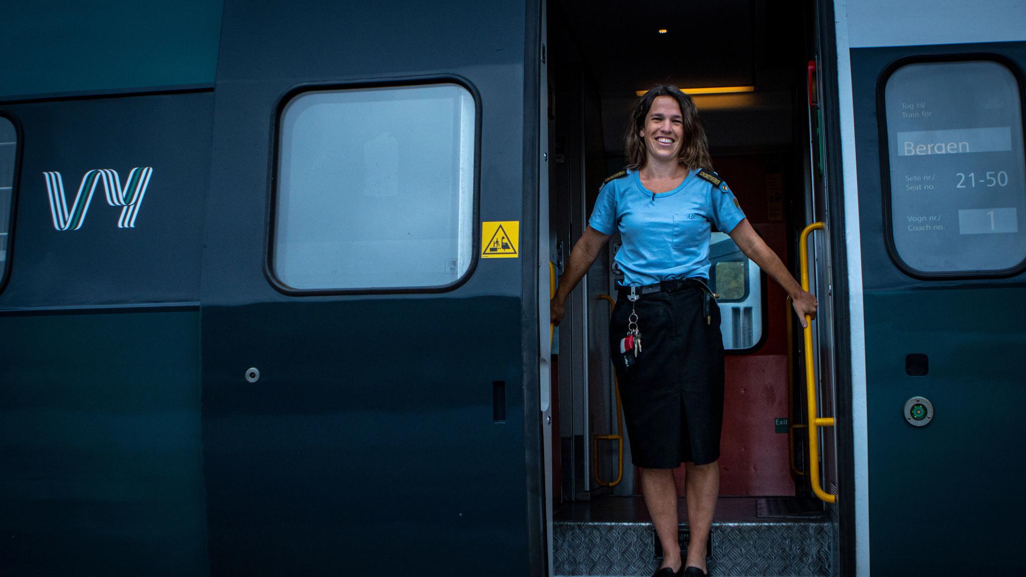 A train driver is standing at the entrance to a train wagon