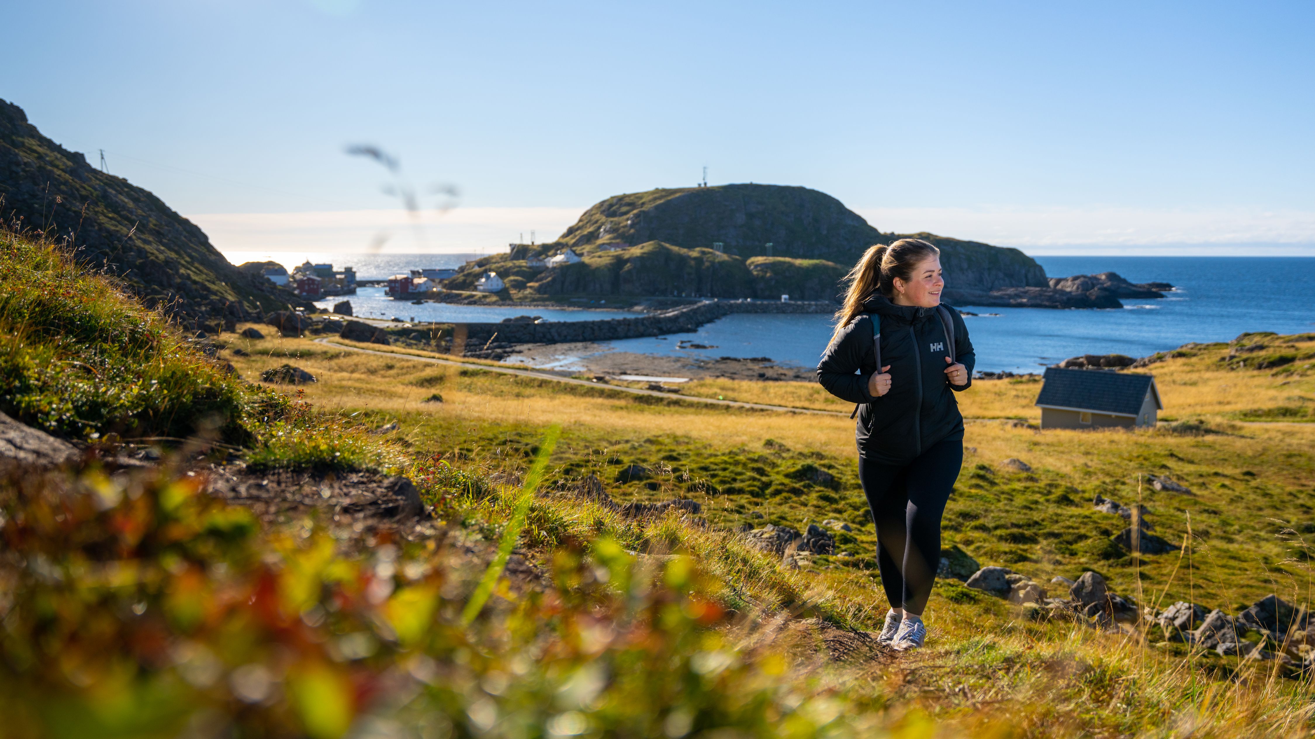 A woman hiking the Dronningruta hiking trail over Nyksund in Vesterålen, Northern Norway