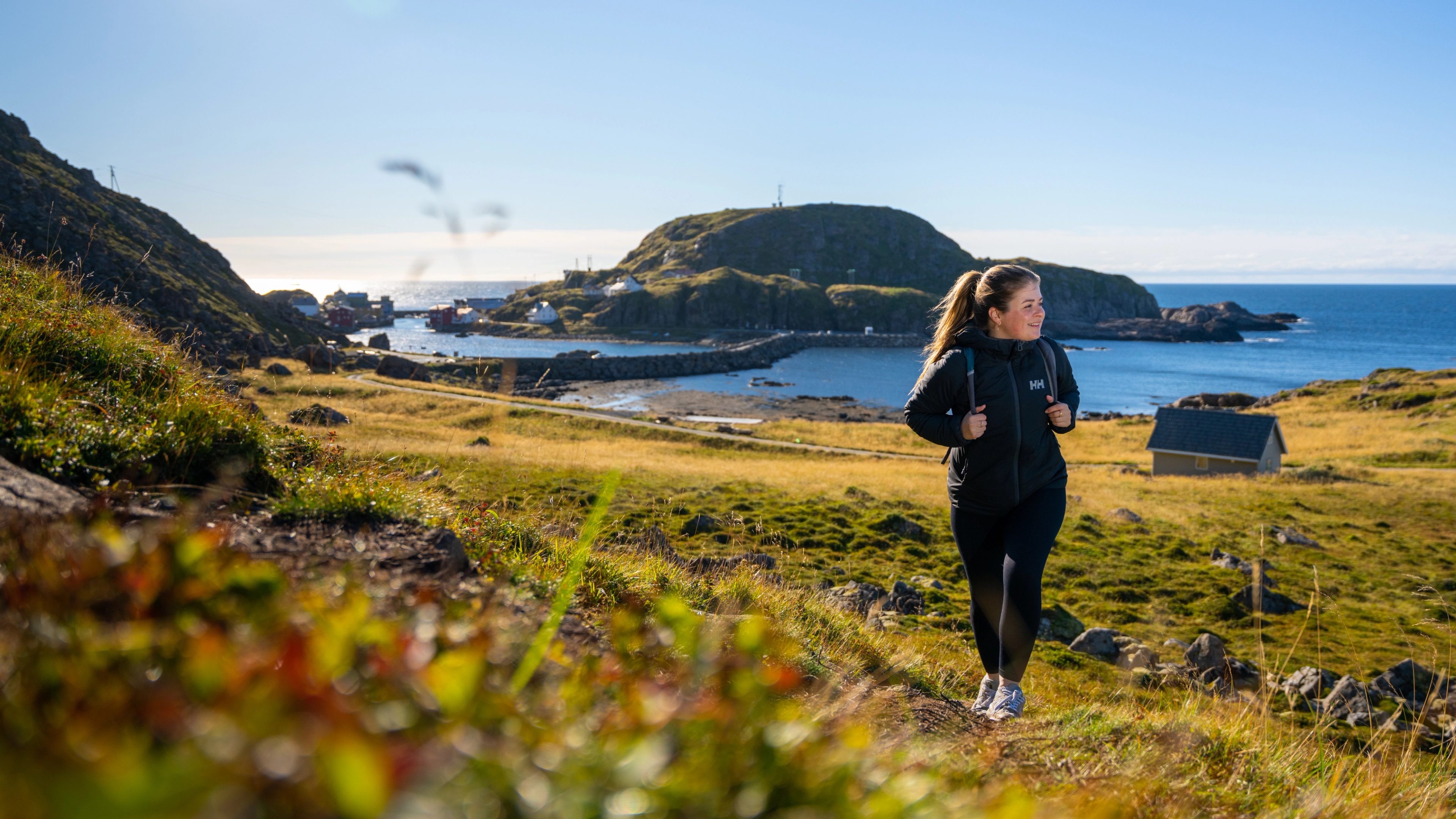 A woman hiking the Dronningruta hiking trail over Nyksund in Vesterålen, Northern Norway