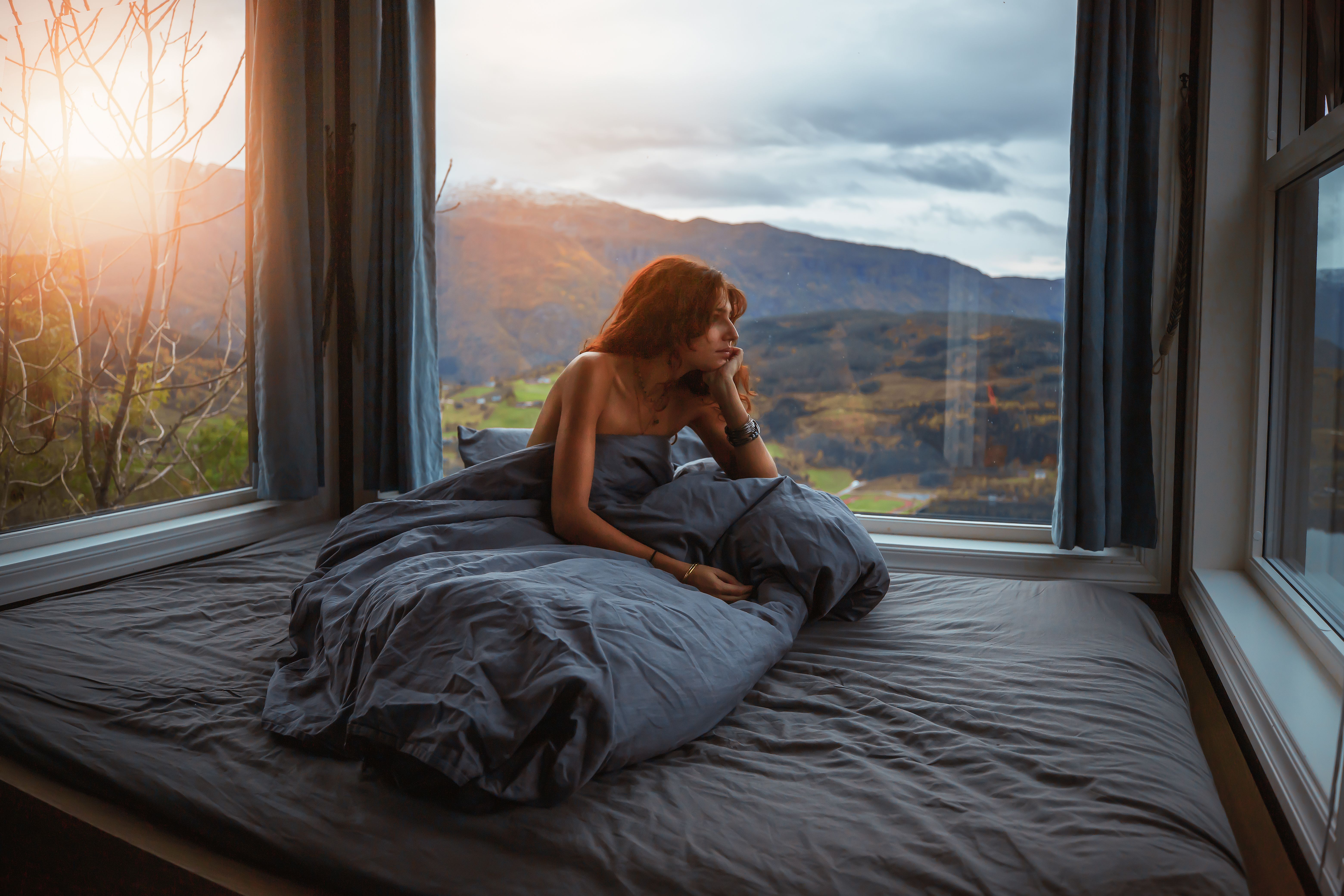 En dame sitter i sengen og ser ut av vinduet fra Hardanger panorama lodge i Hardanger