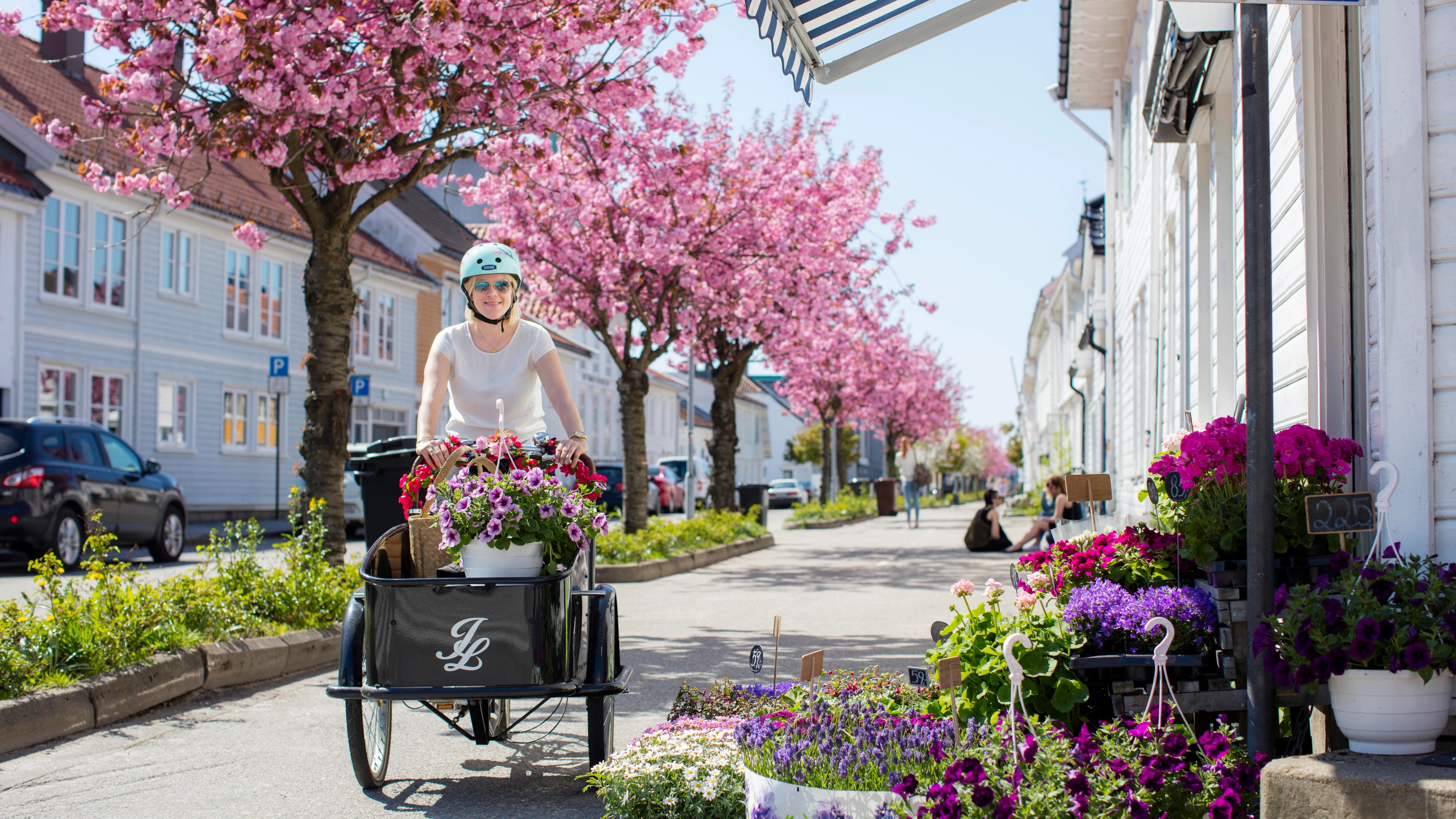 A woman cycling through Posebyen in Kristiansand on a transport bike full of flowers. Southern Norway.