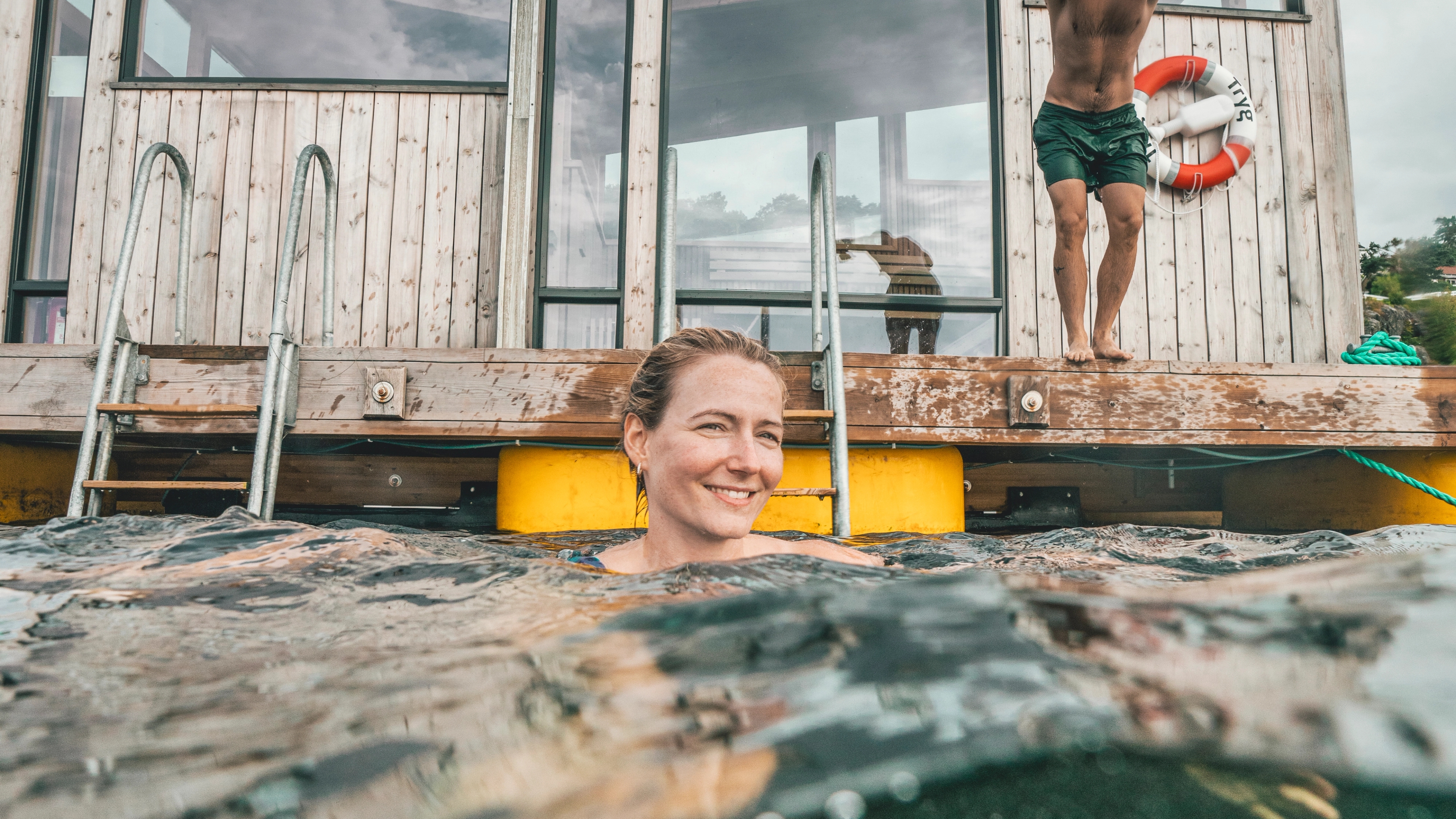 En kvinne bader og en mann er i ferd med å hoppe uti, på Risør havbad på Sørlandet