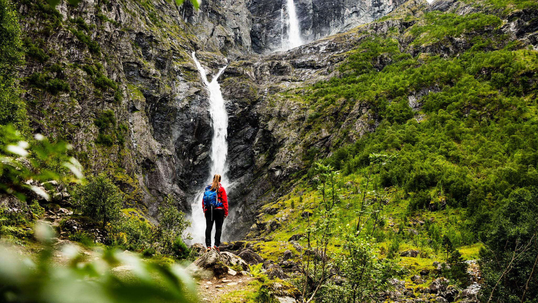 A woman is standing in front of the Mardalsfossen waterfall in Molde during summer. Northwest, Fjord Norway.