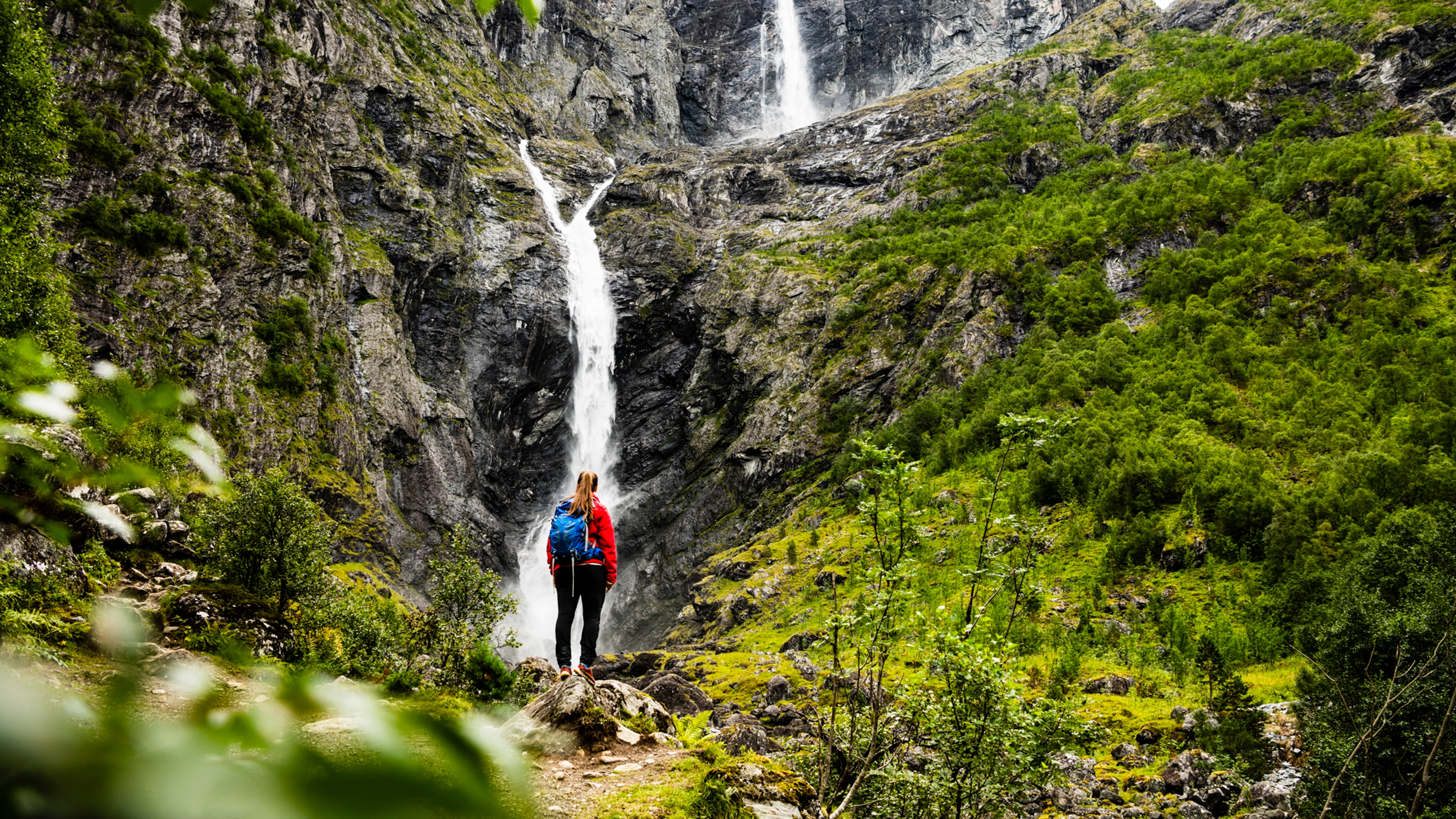 A woman is standing in front of the Mardalsfossen waterfall in Molde during summer. Northwest, Fjord Norway.