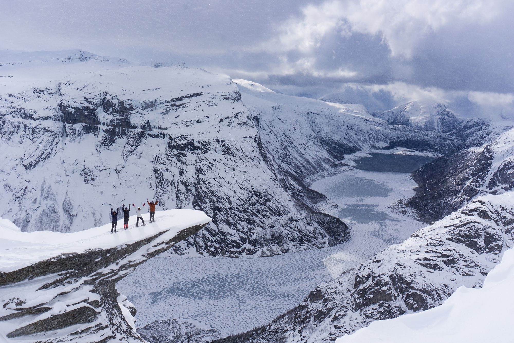 Un grupo de cuatro personas con raquetas de nieve disfruta las vistas desde lo alto de Trolltunga, en la Noruega de los fiordos, en un día de invierno.