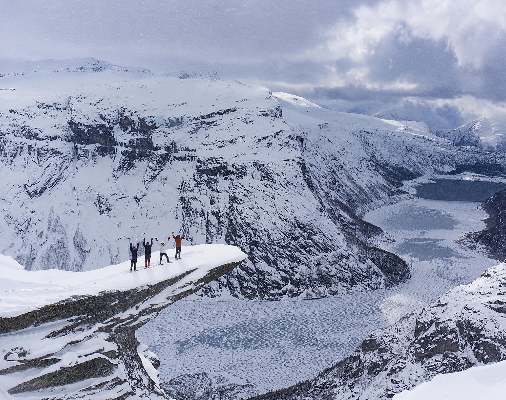 Fire personer står på Trolltunga med snesko om vinteren