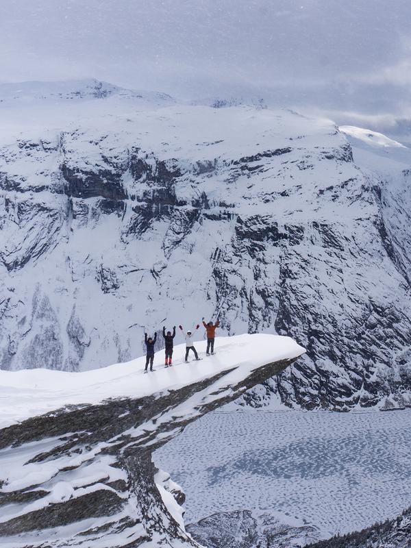 Un grupo de cuatro personas con raquetas de nieve disfruta las vistas desde lo alto de Trolltunga, en la Noruega de los fiordos, en un día de invierno.