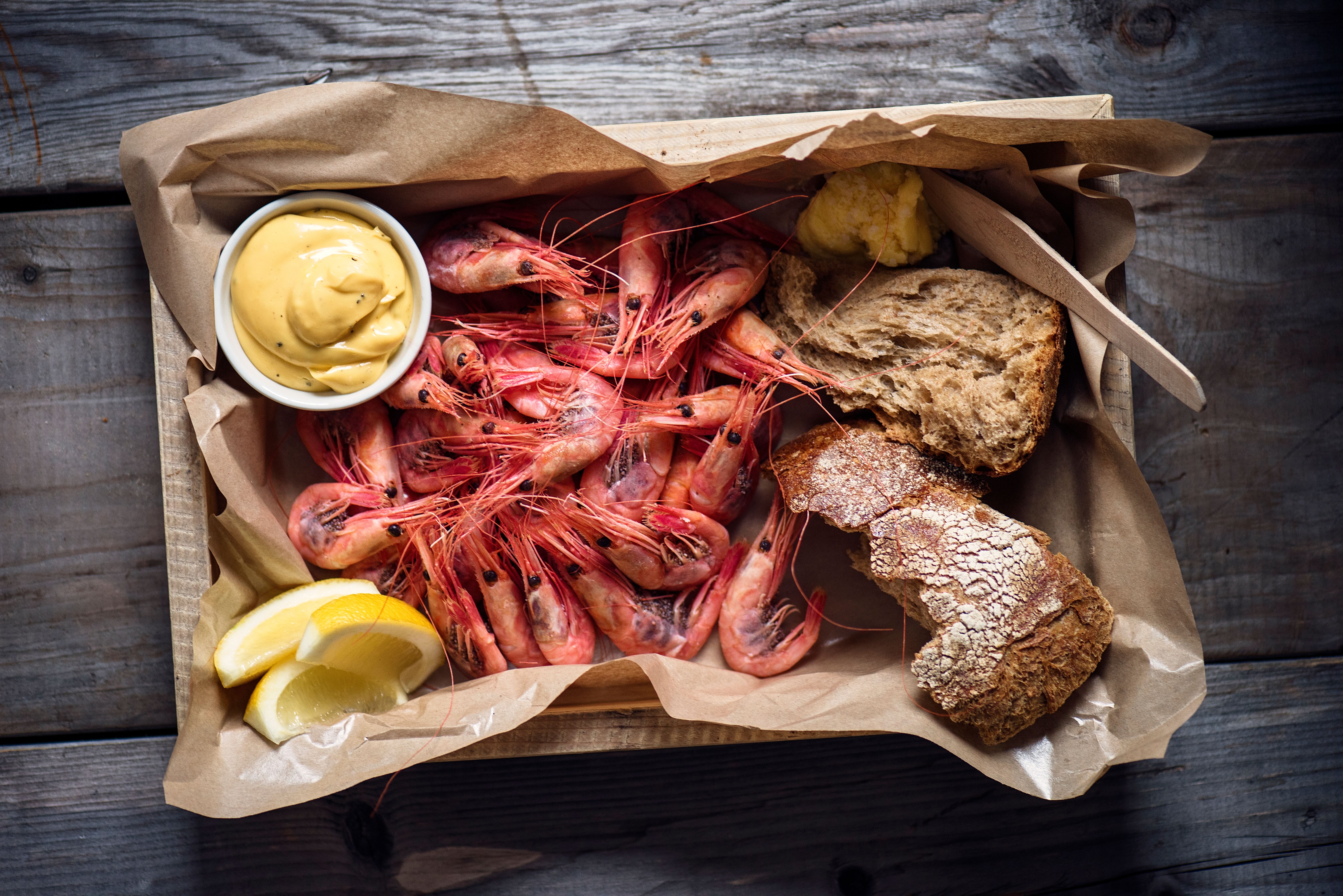 Shrimp in a wooden box accompanied by lemon wedges and sauce