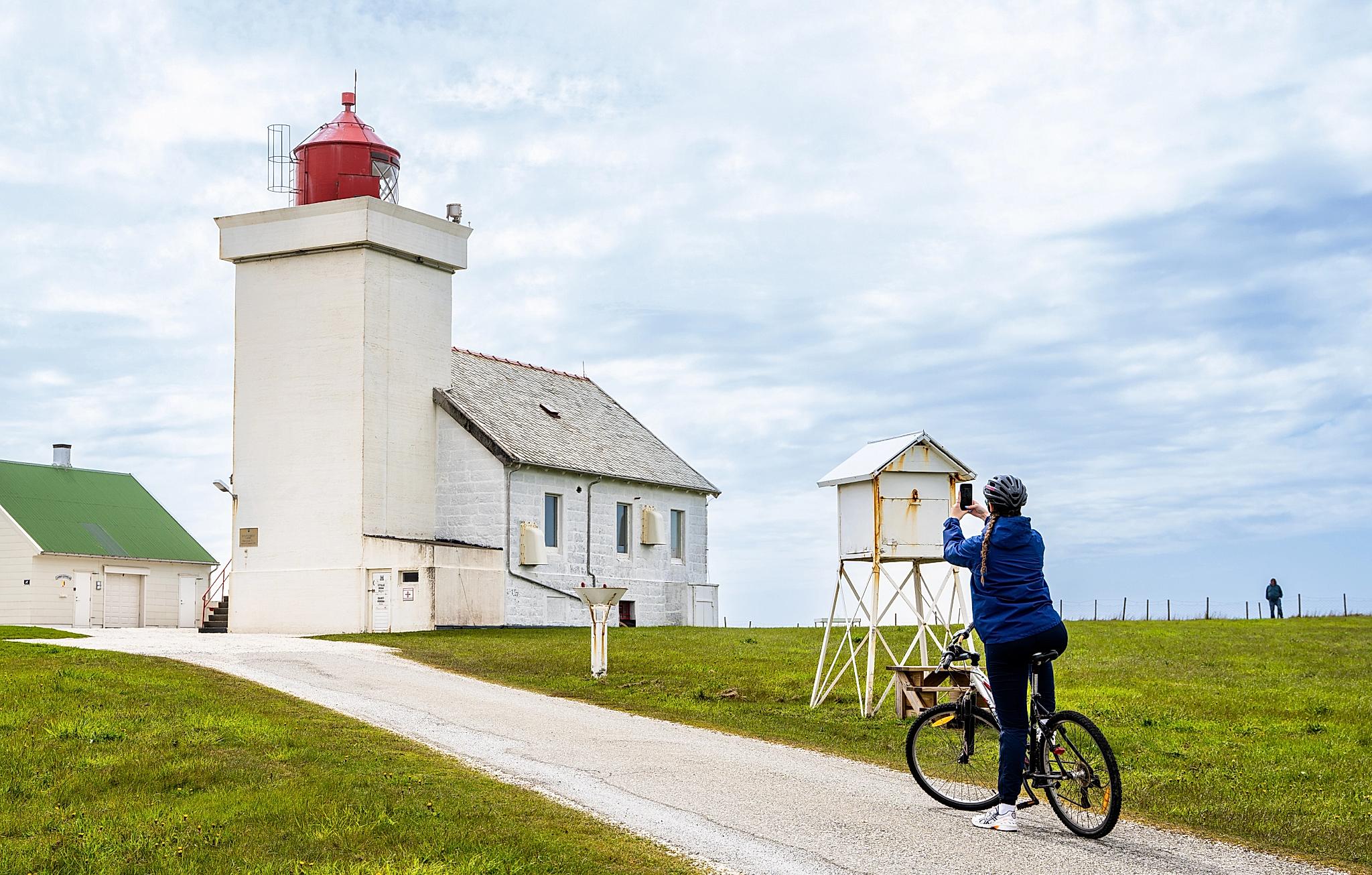 A woman taking a picture of the Obrestad lighthouse at the Jæren coast, Fjord Norway.