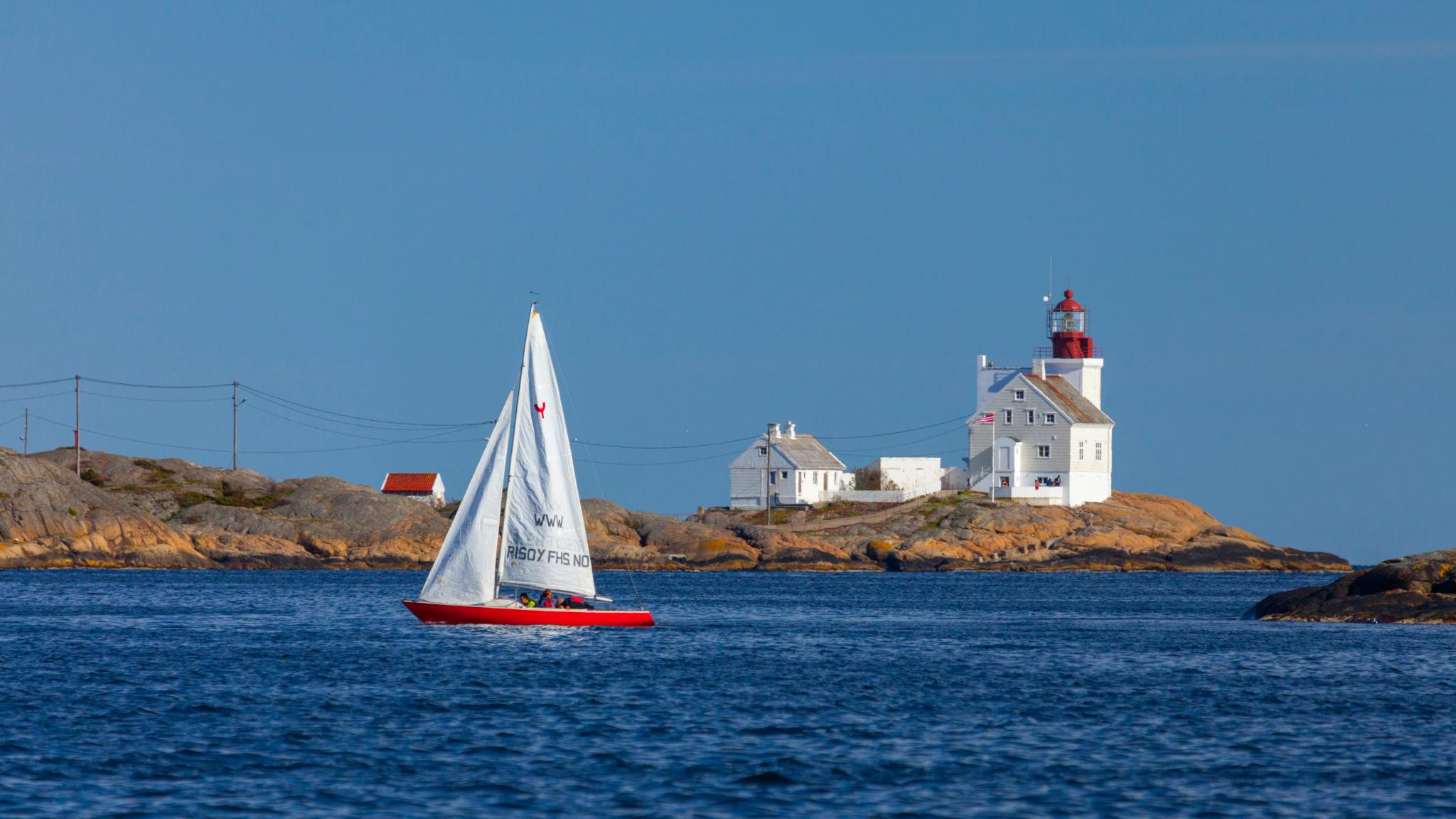 A sailboat passing by the Lyngør lighthouse during summer in Southern Norway.