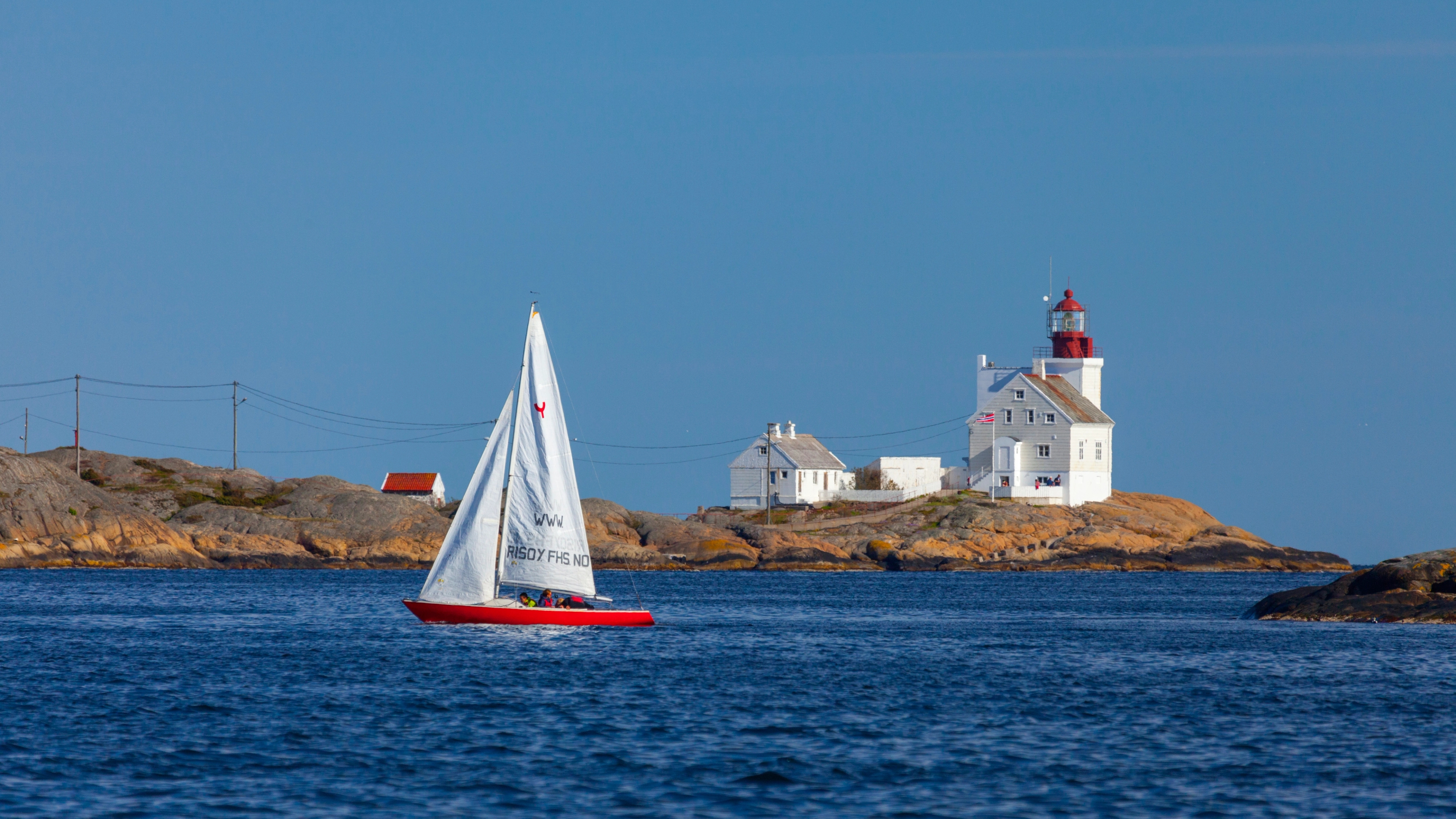 A sailboat passing by the Lyngør lighthouse during summer in Southern Norway.