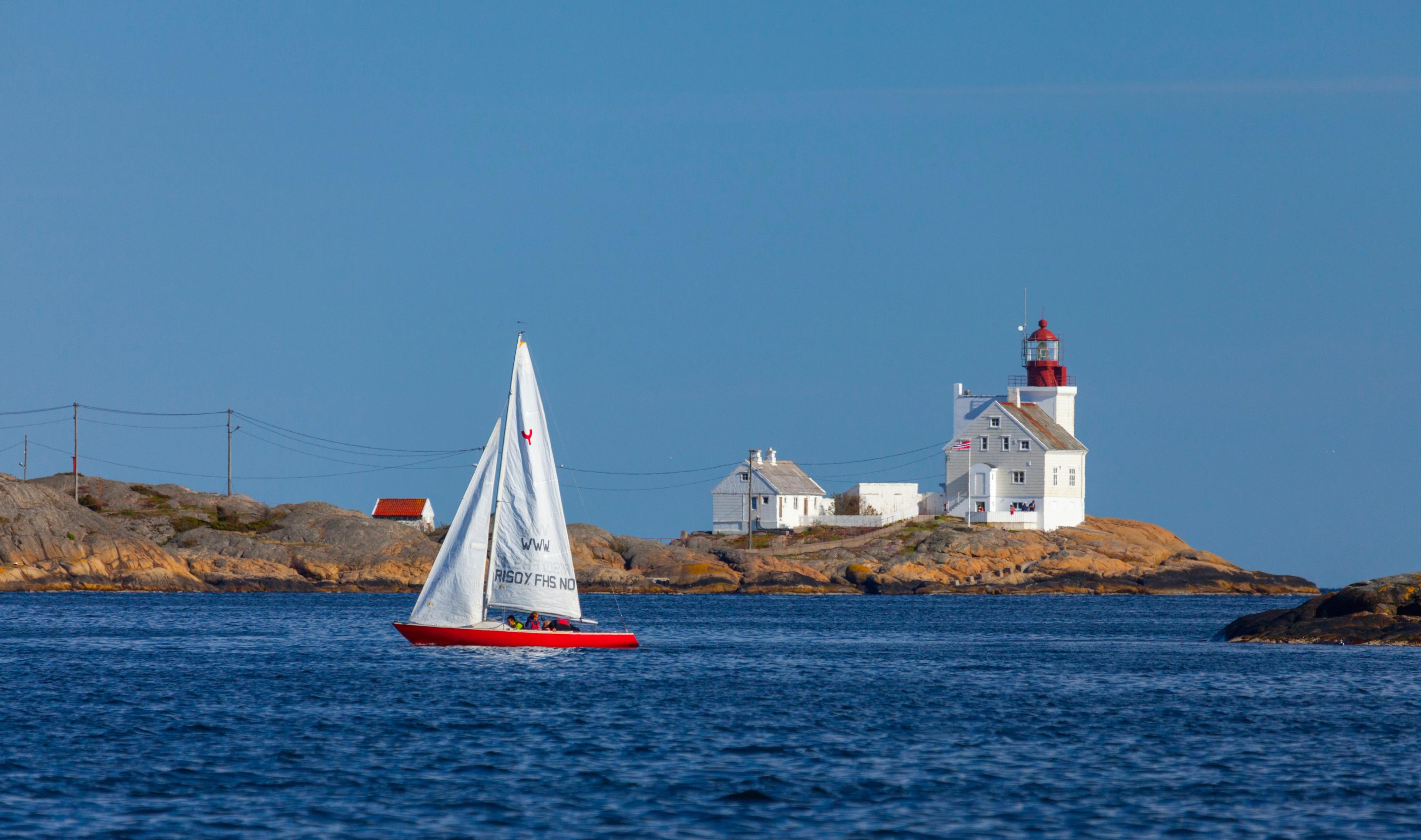 A sailboat passing by the Lyngør lighthouse during summer in Southern Norway.