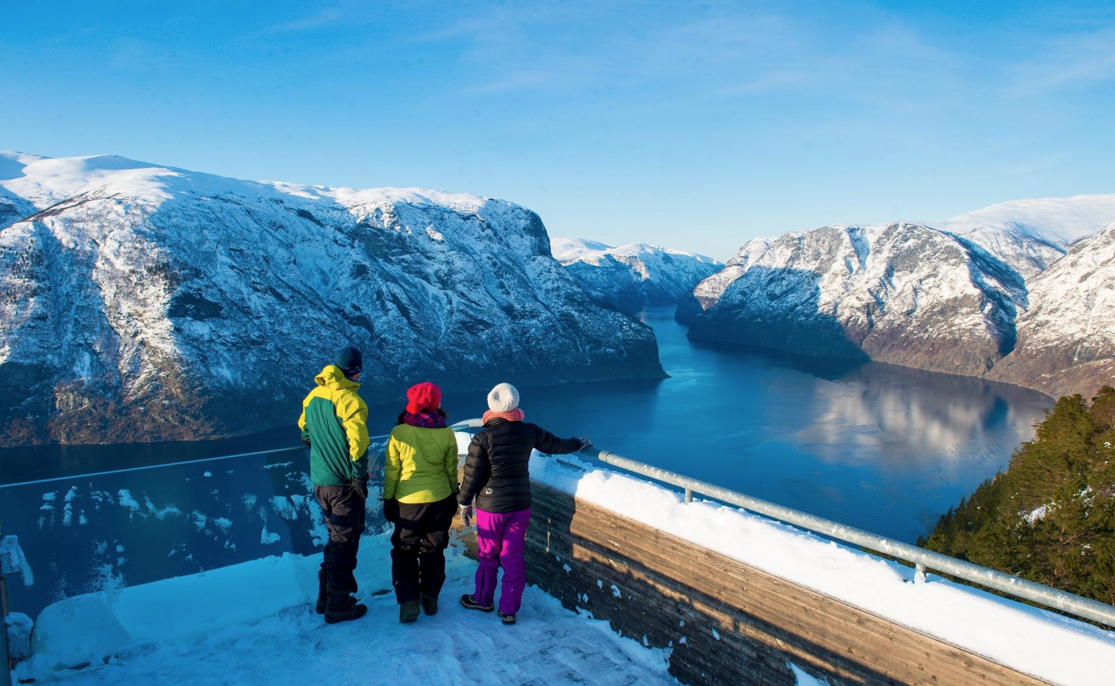 Three people at a snowy mountain viewpoint overlooking Sognefjord