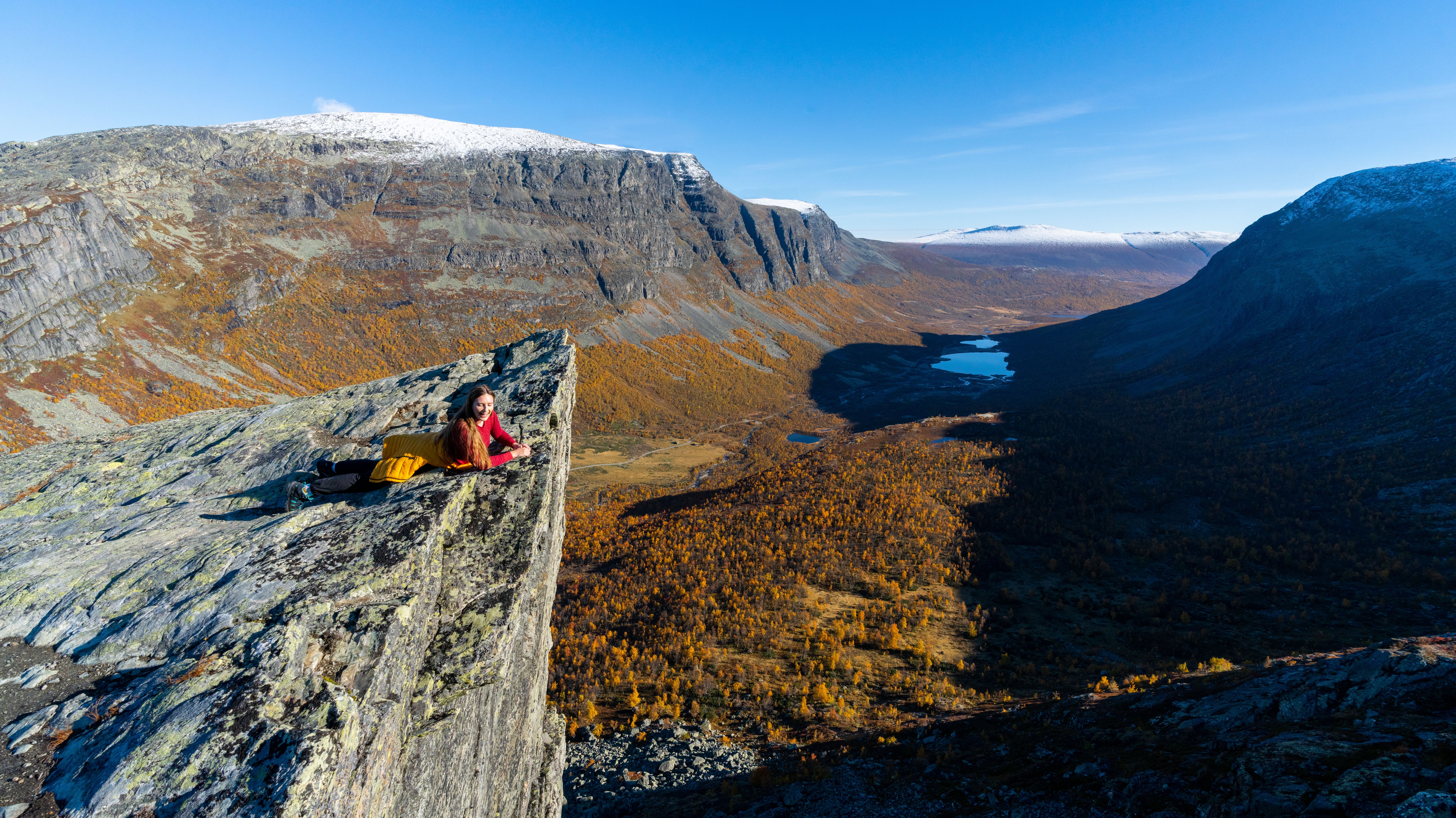 A woman overlooking mountains in autumn colours form a cliff.