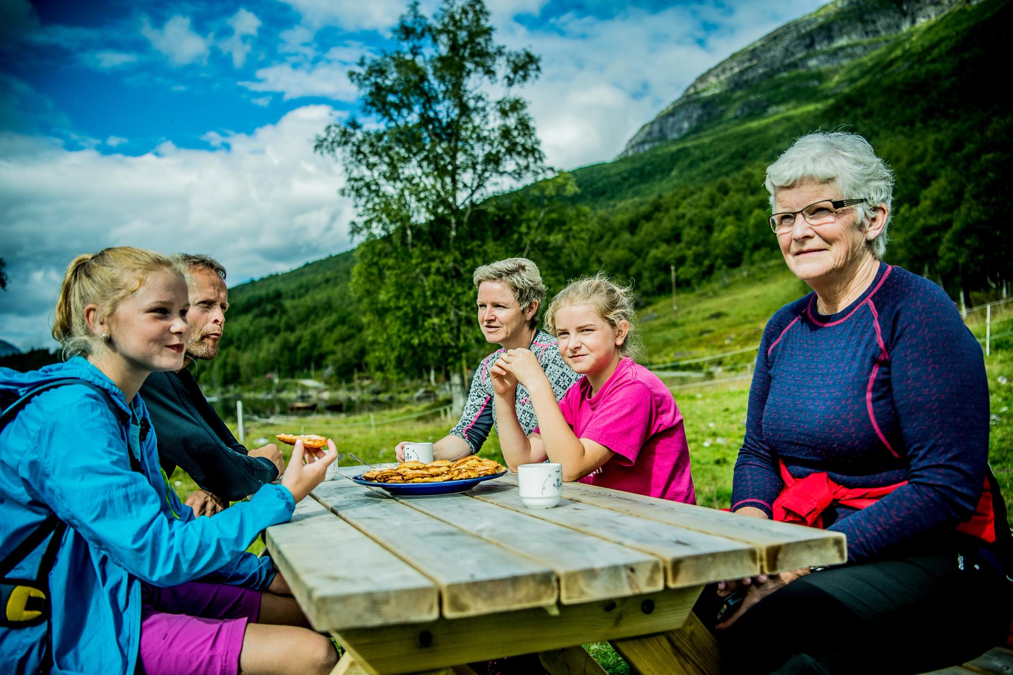 A family of five sitting at a wooden table outside, eating waffles