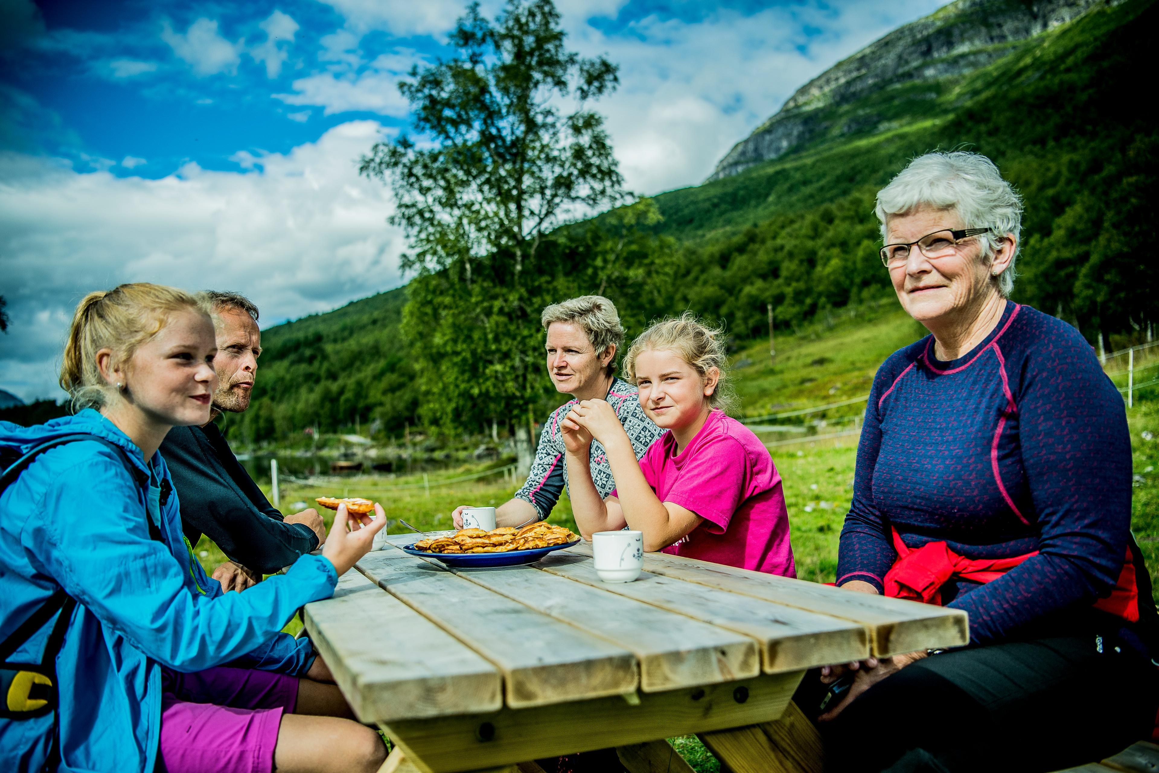 A family of five sitting at a wooden table outside, eating waffles