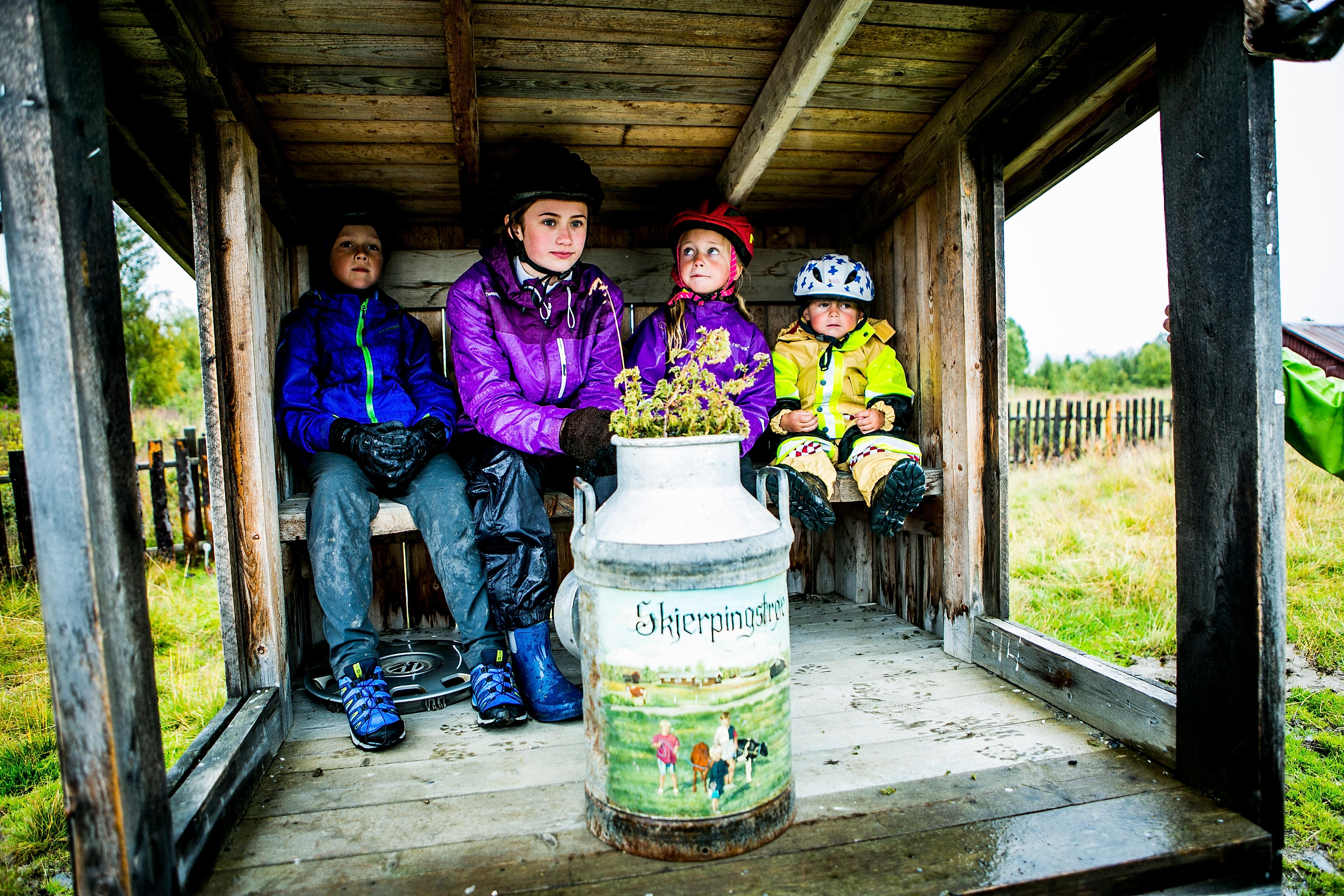 Four children sitting in a small house for unloading milk at Mjølkevegen in Valdres, Eastern Norway